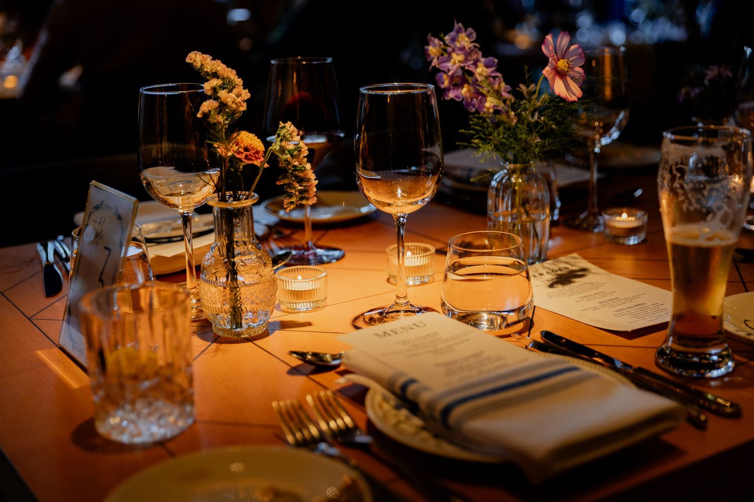 Elegant table settings with wine glasses and floral centerpieces in warm candlelight.
