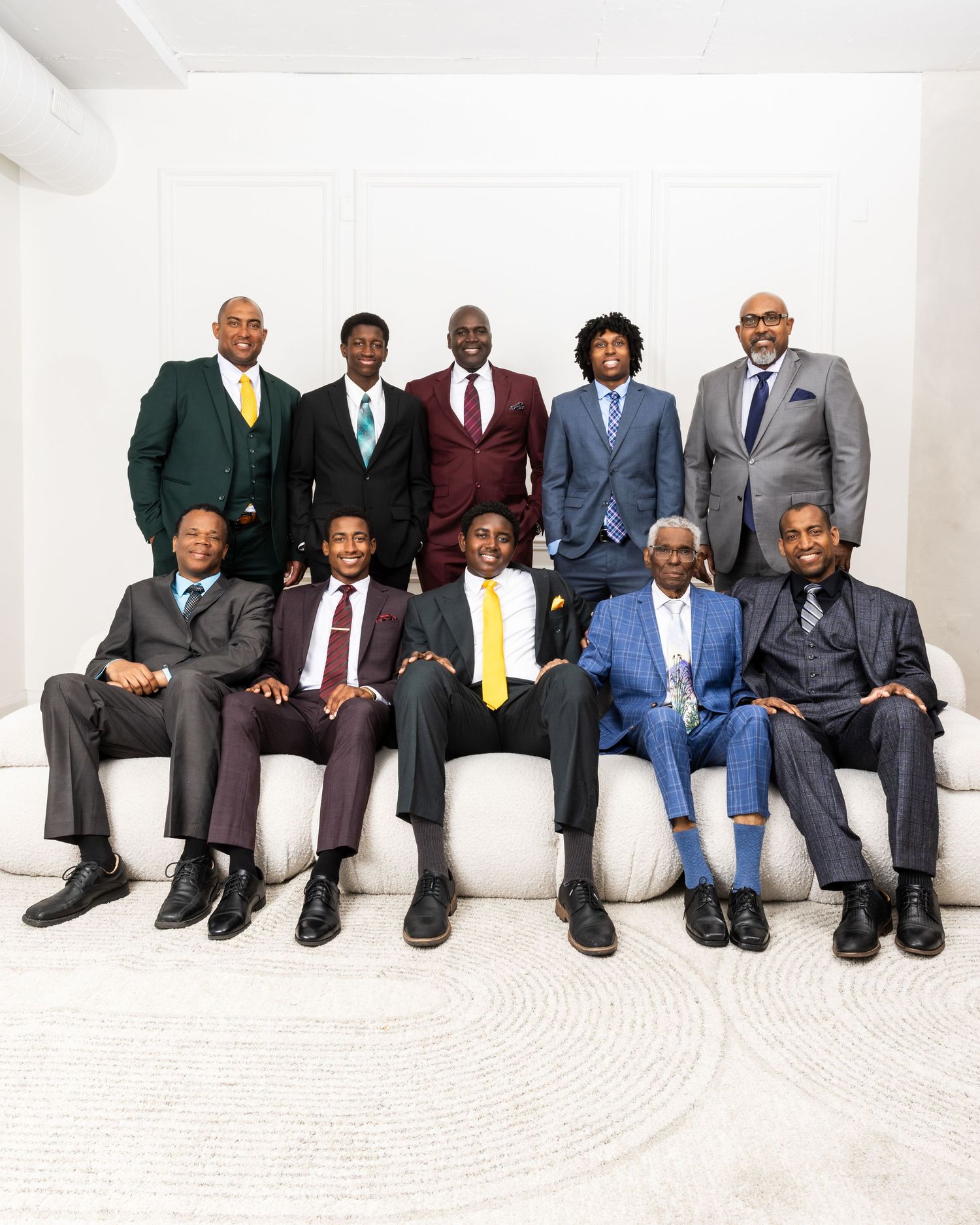 Professional men in business suits seated in a row against a white wall.