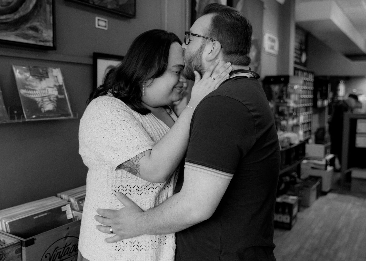 Black and white photo of a couple sharing a tender kiss in a cozy bookstore, embracing romantically.