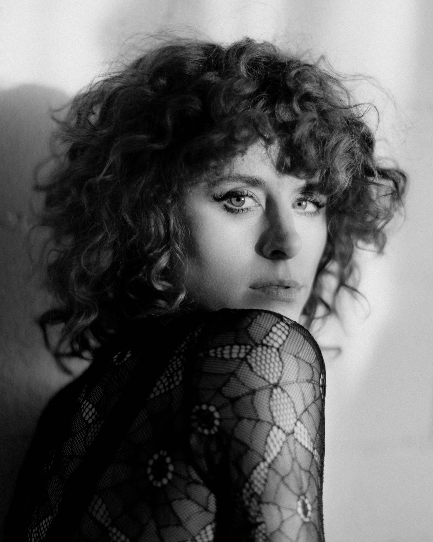 Dramatic black and white portrait in lace sleeve with curly hair and expressive eyes.