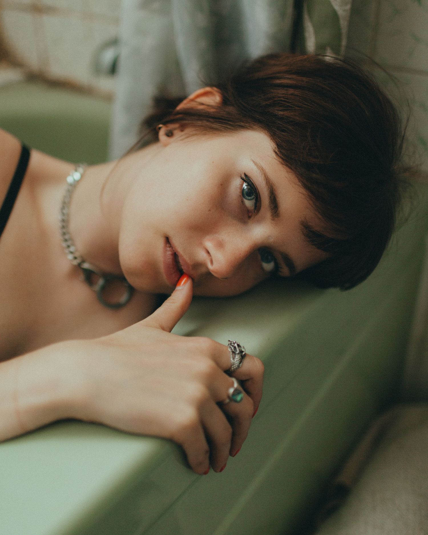 Intimate portrait with jewelry and short dark hair against green background.