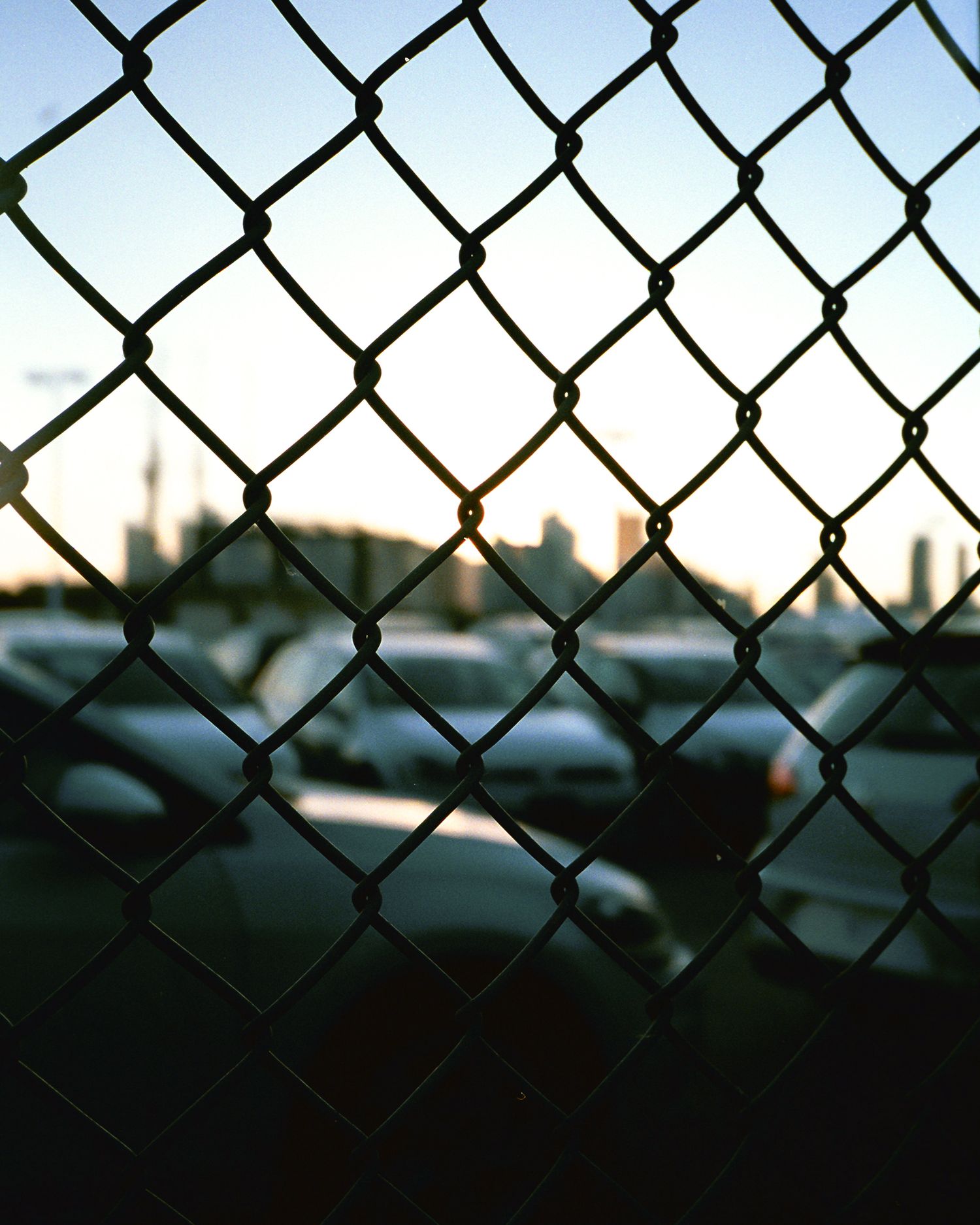 Chain-link fence silhouetted against a blurry urban background at dusk.