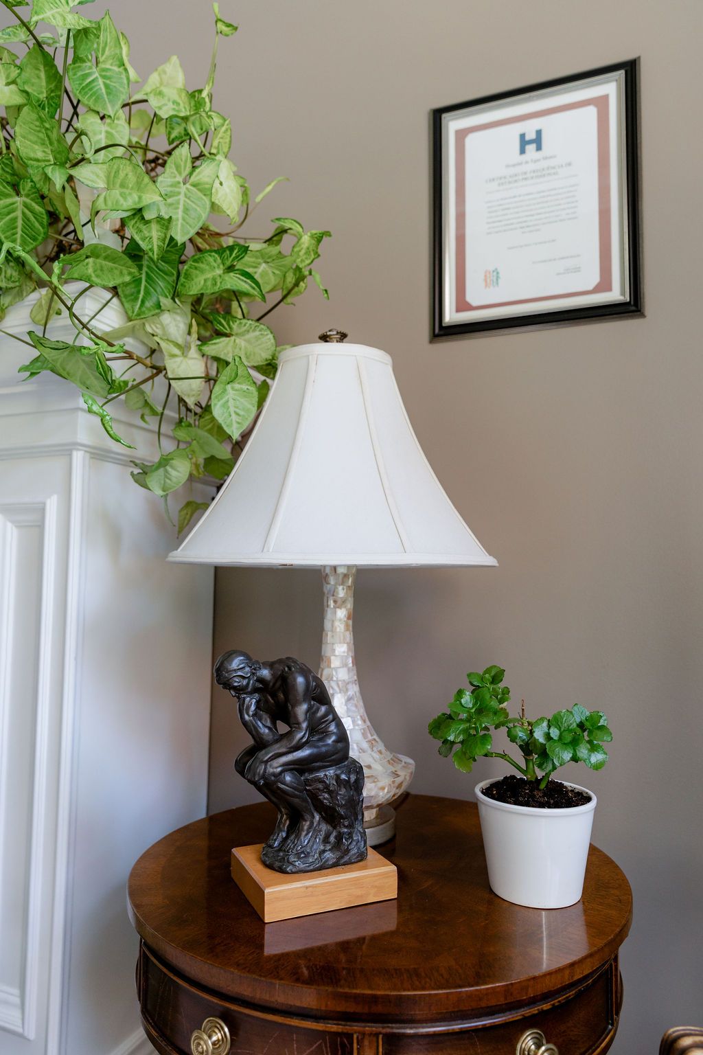 Elegant side table with The Thinker lamp, small potted plant, and framed certificate on gray wall.