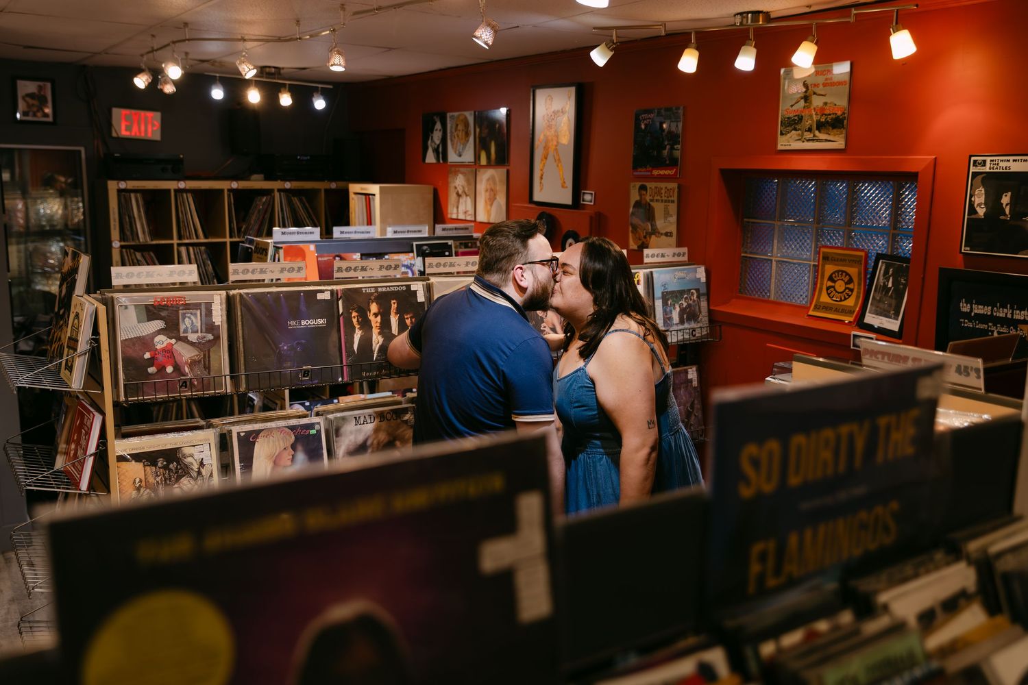 Couple sharing a romantic kiss in a cozy record store surrounded by vinyl albums on display shelves.