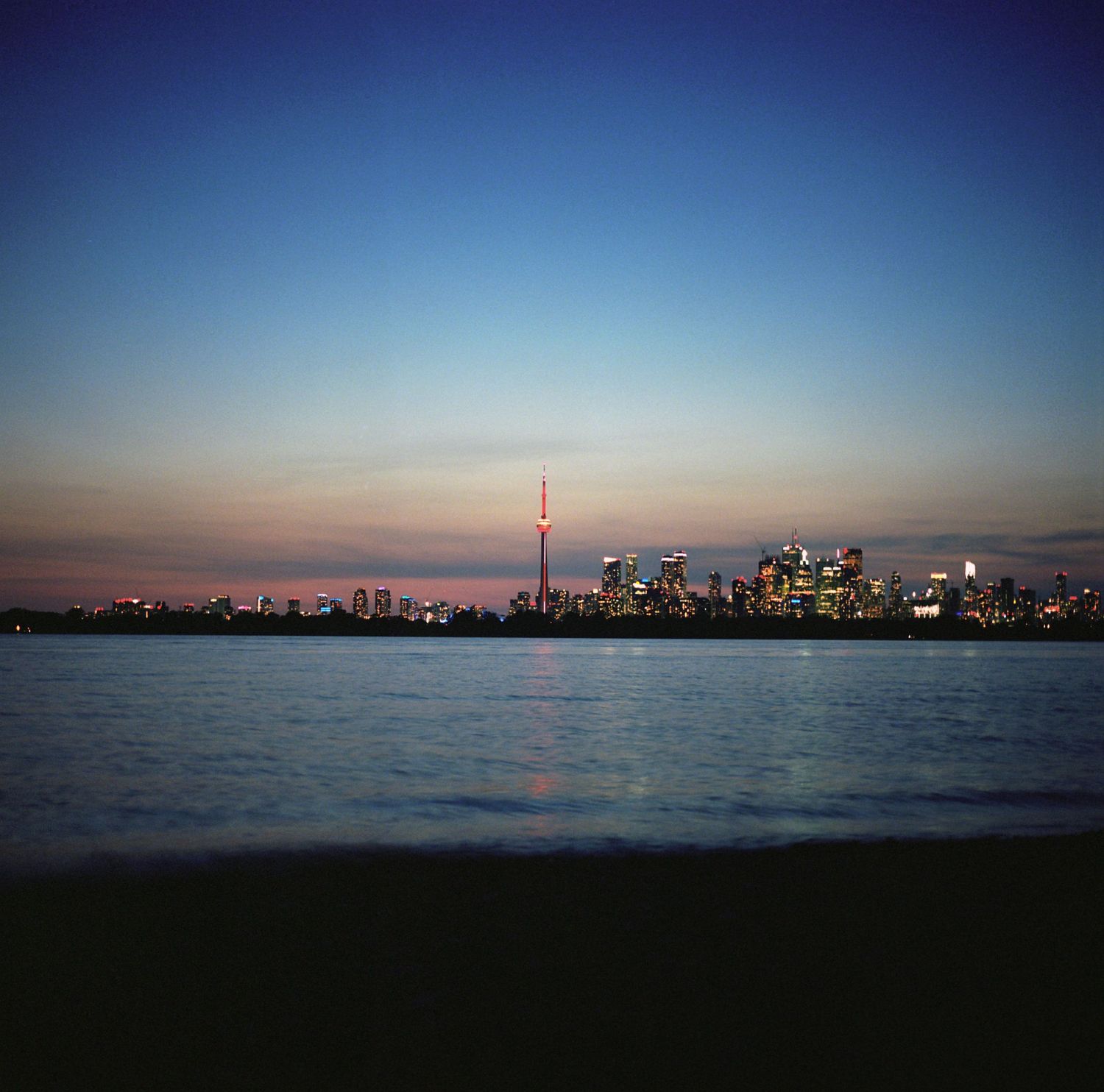 Panoramic cityscape silhouette at dusk reflecting over calm water.