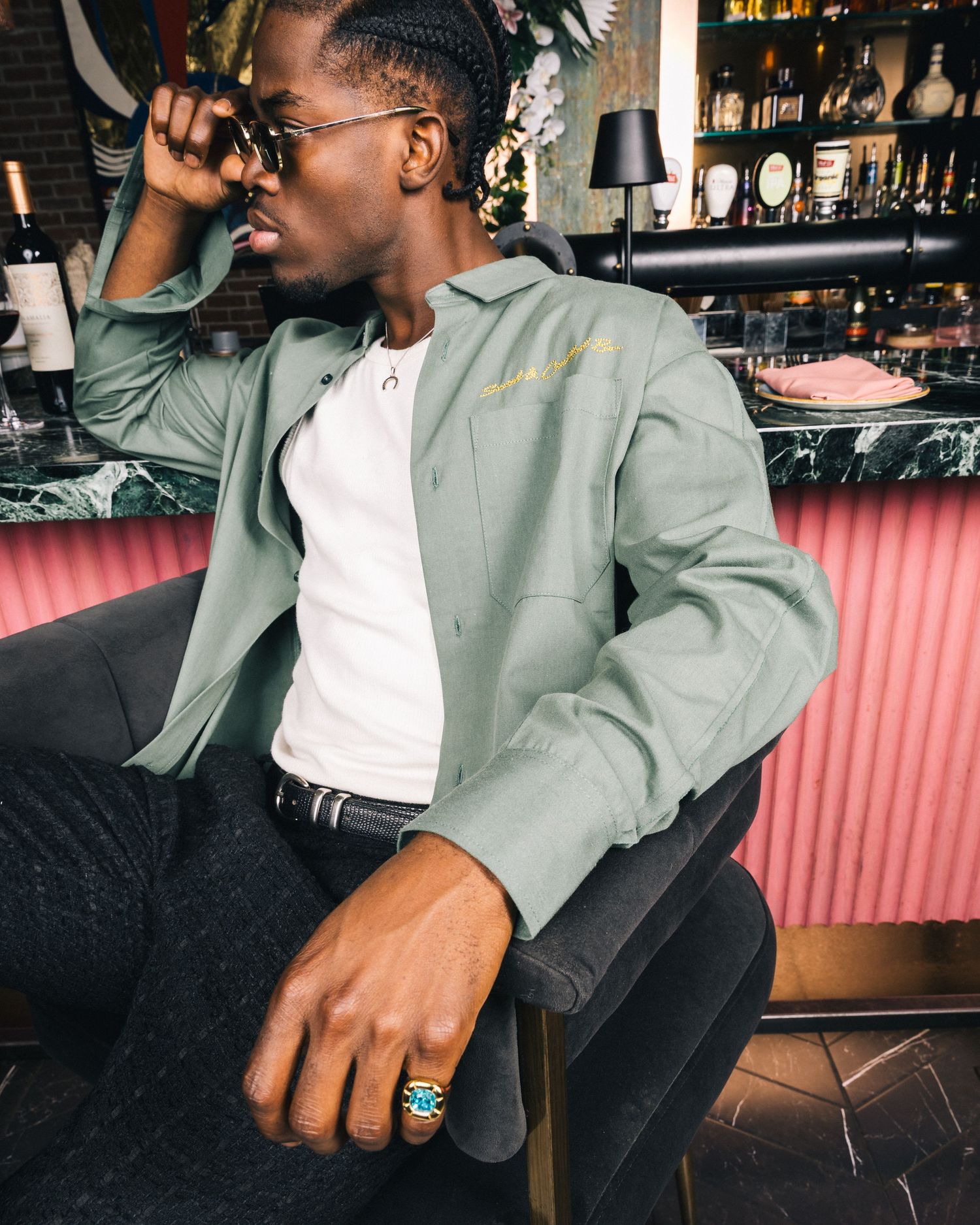 Close-up of person seated at bar wearing sage green jacket and dark pants.