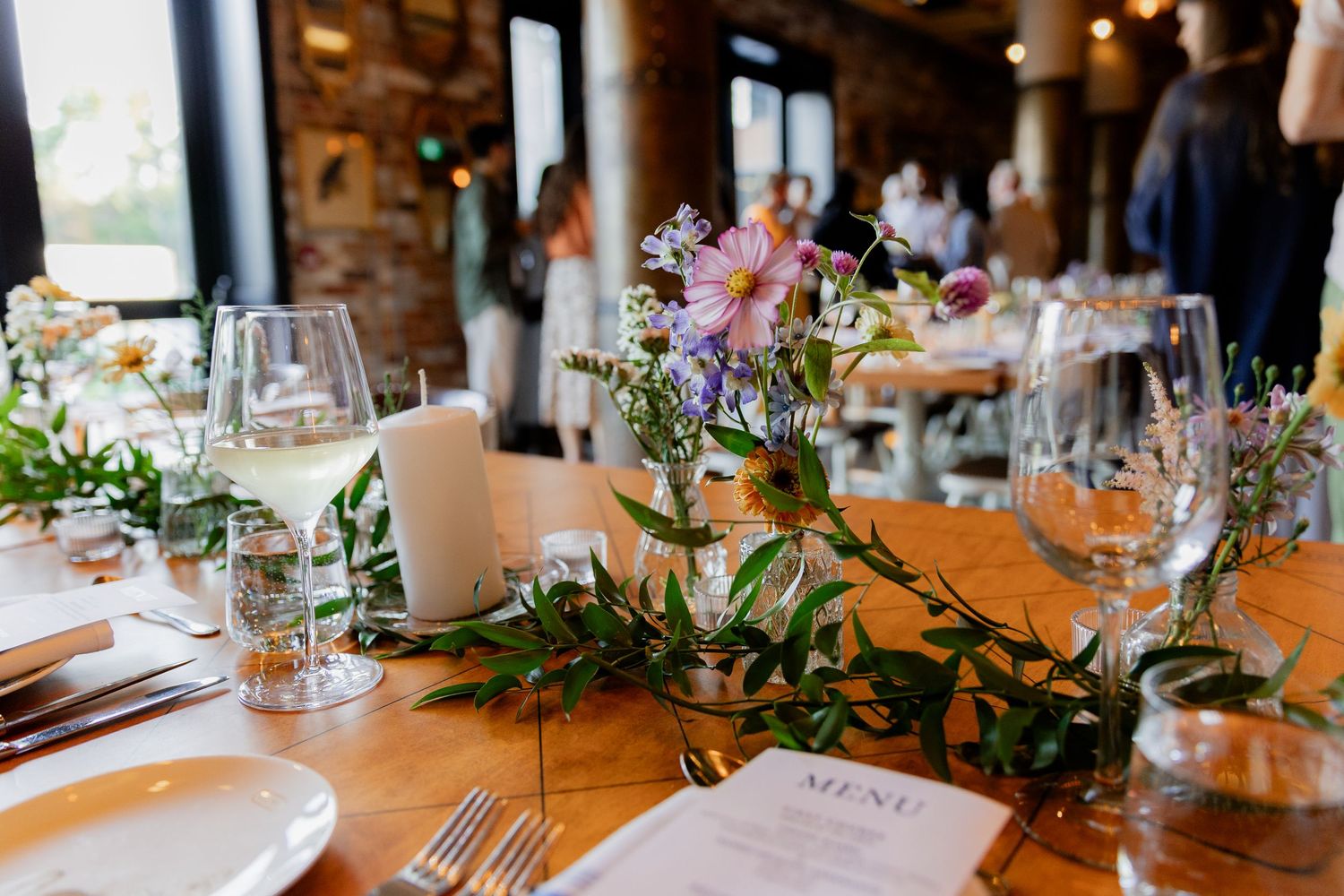 Elegant table setting with floral centerpieces, wine glasses, and menu cards at a wedding reception.