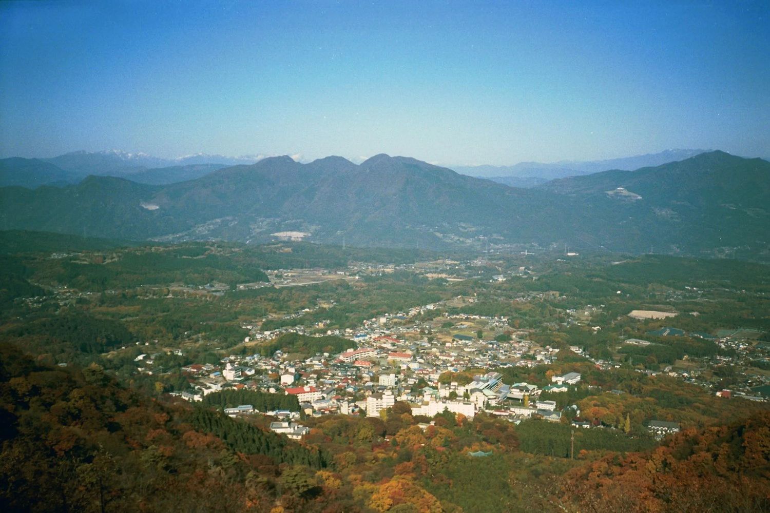Panoramic aerial view of a city nestled in mountainous terrain under blue skies.
