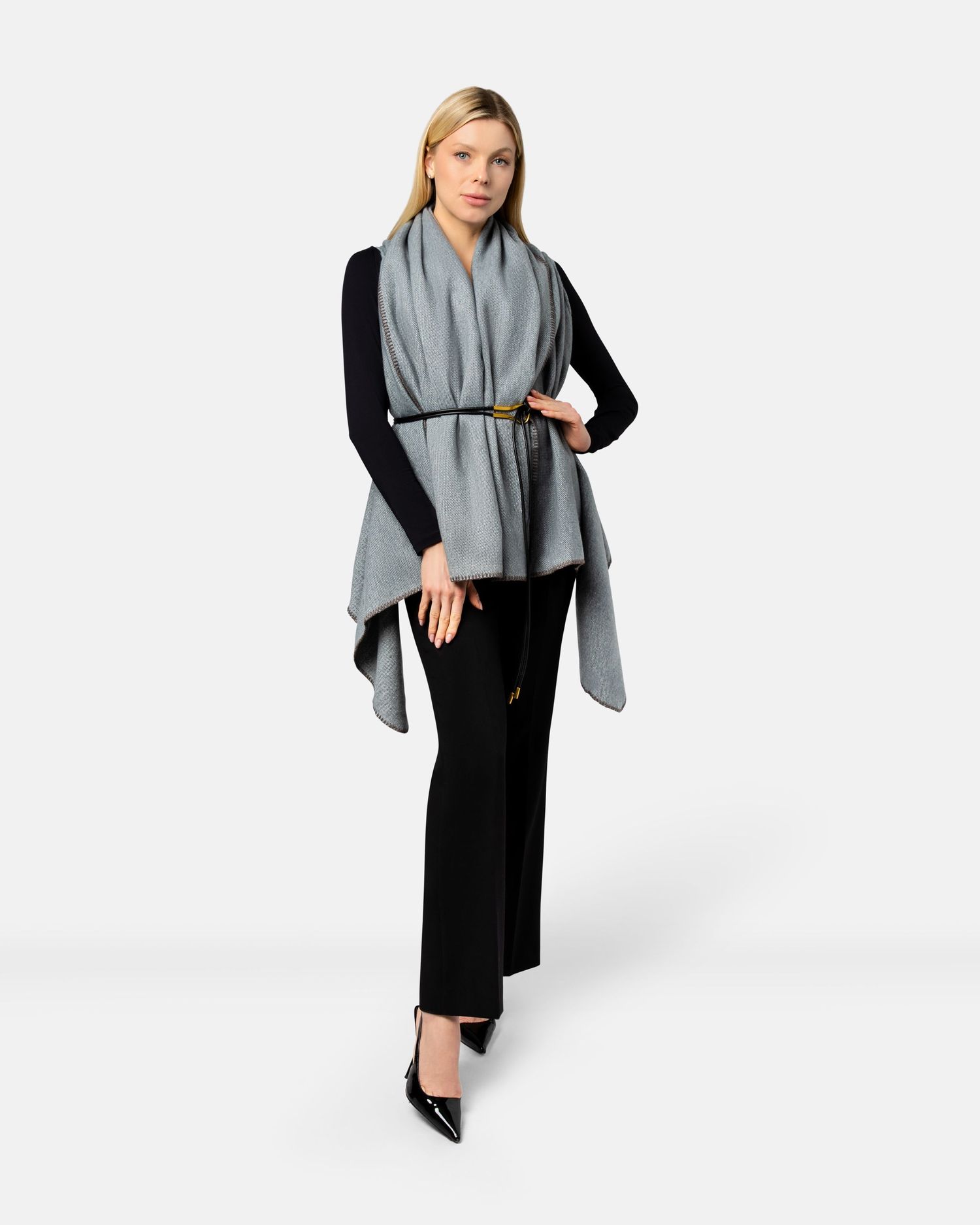 A model wearing a grey draped shawl over a black dress showcases modern minimalist fashion against a white background.