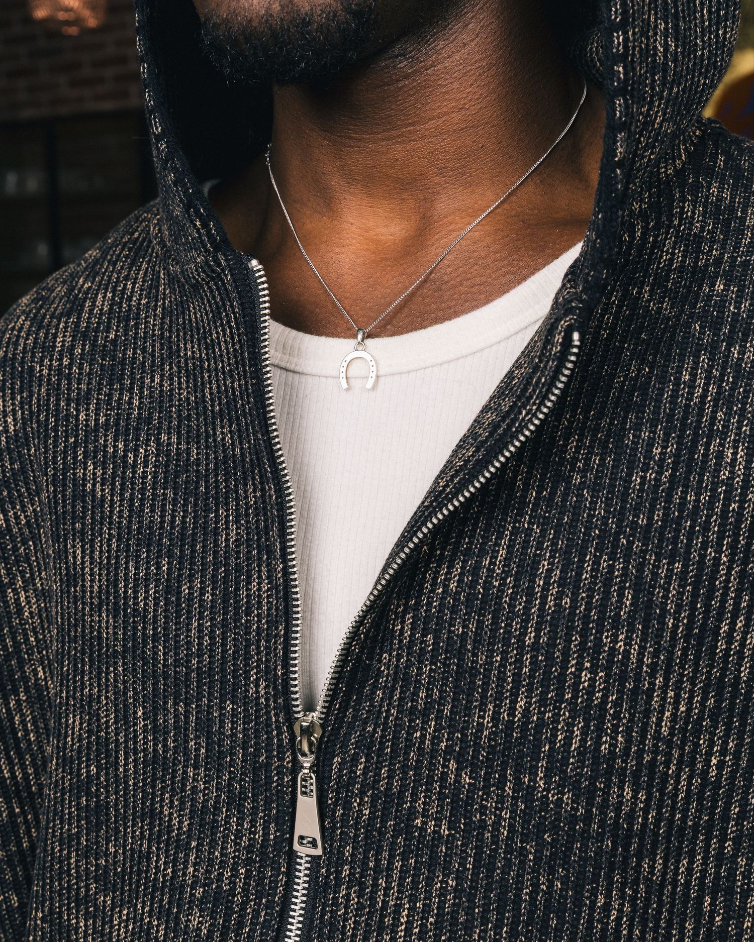 Close-up of person wearing dark ribbed zip-up sweater and white t-shirt.