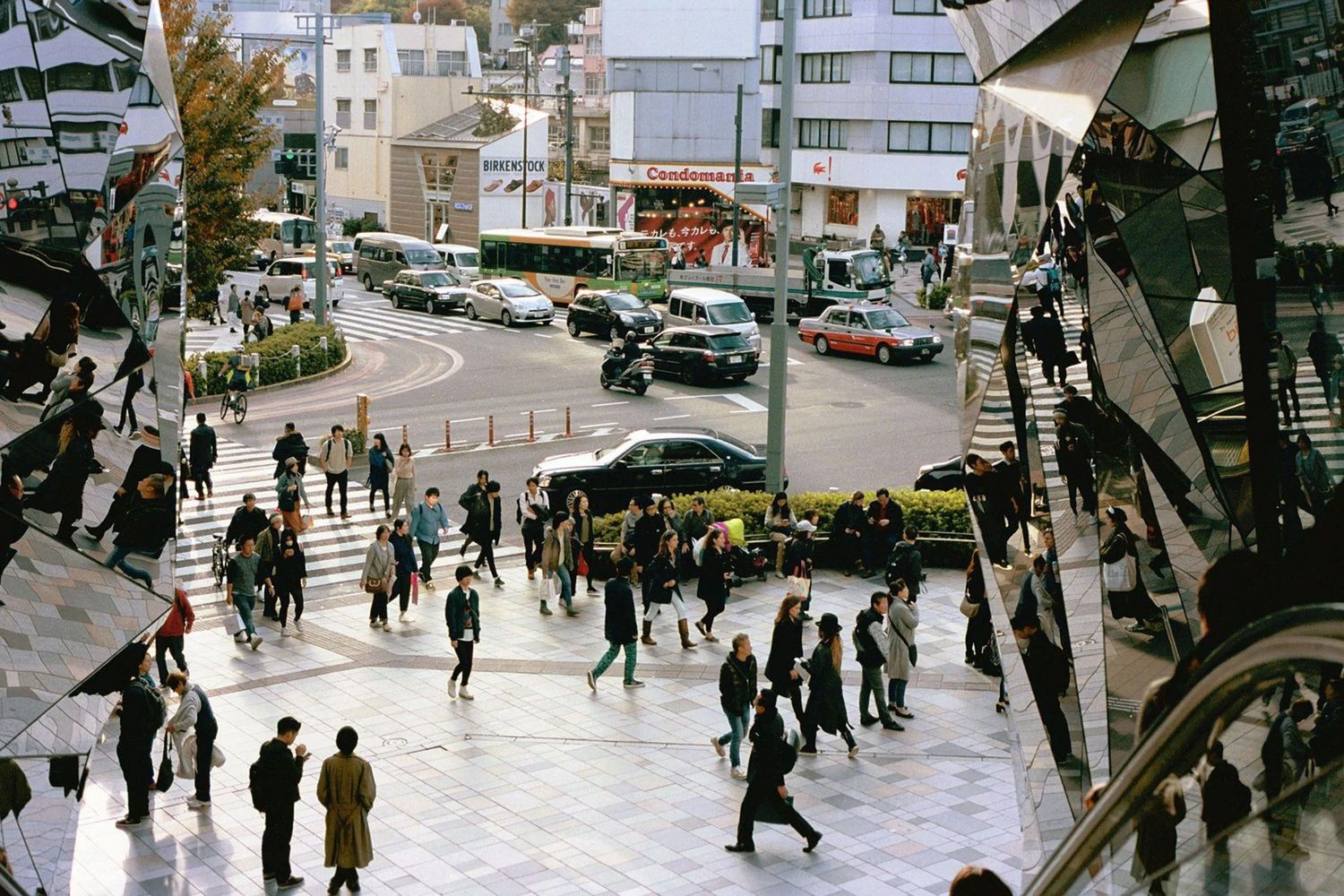 Crowded city street with people walking past shops and buildings.