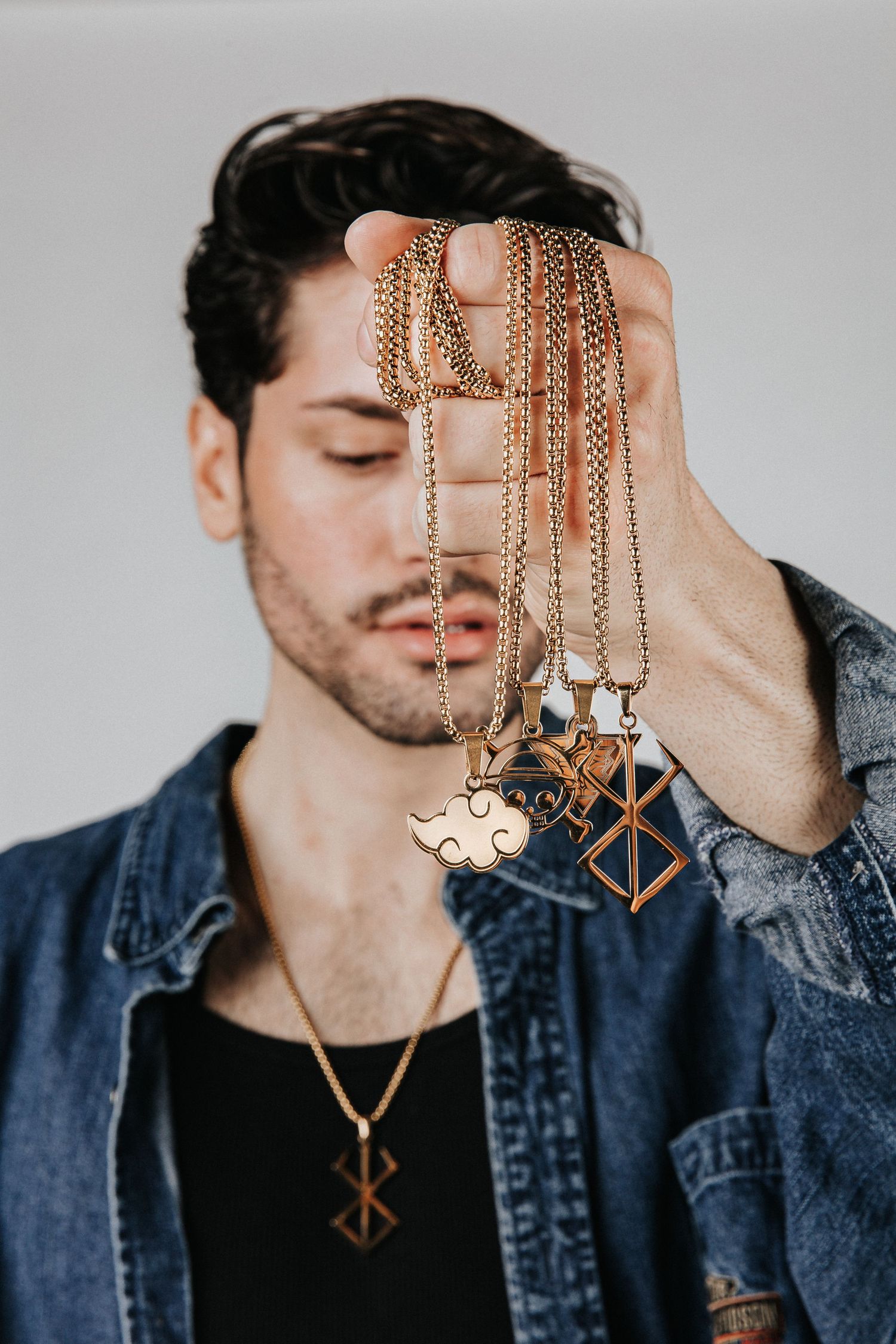 Hand holding gold chain necklaces with geometric pendants against studio background.