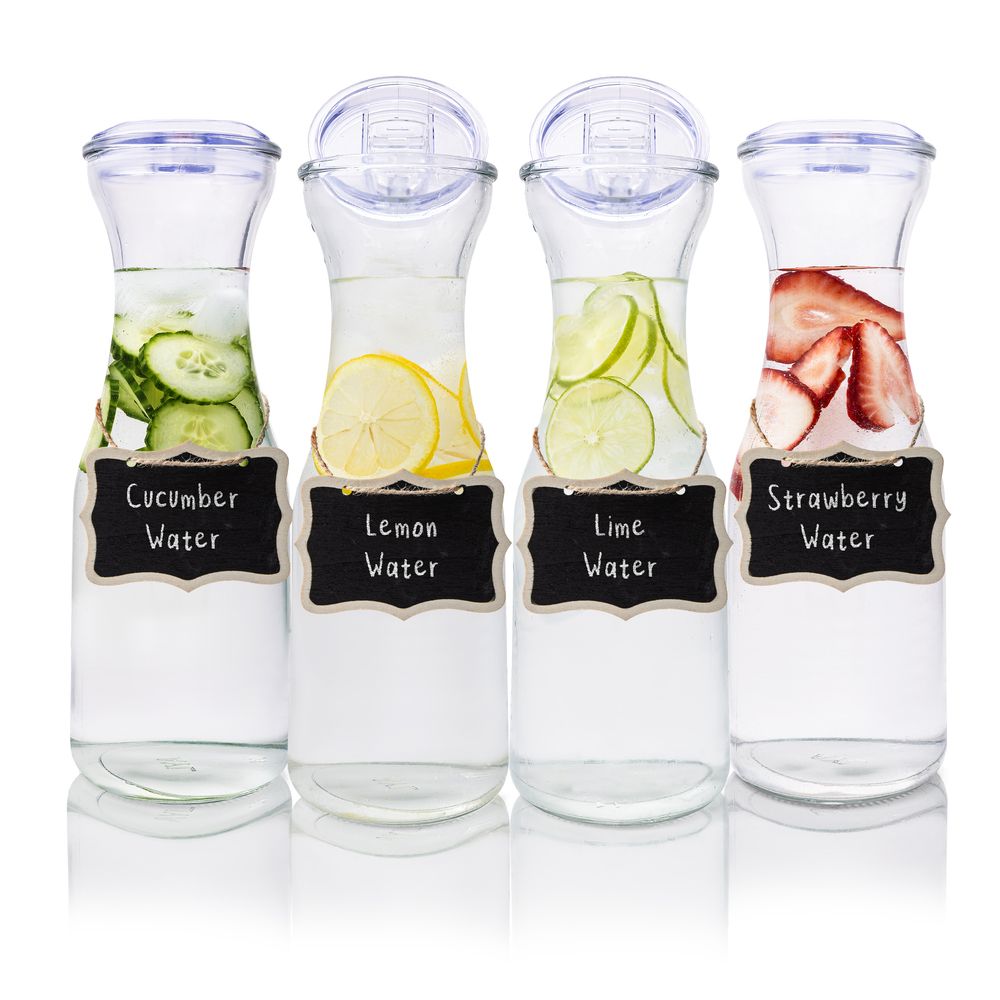 Row of labeled glass carafes containing infused water with cucumber, lemon, lime and strawberry.