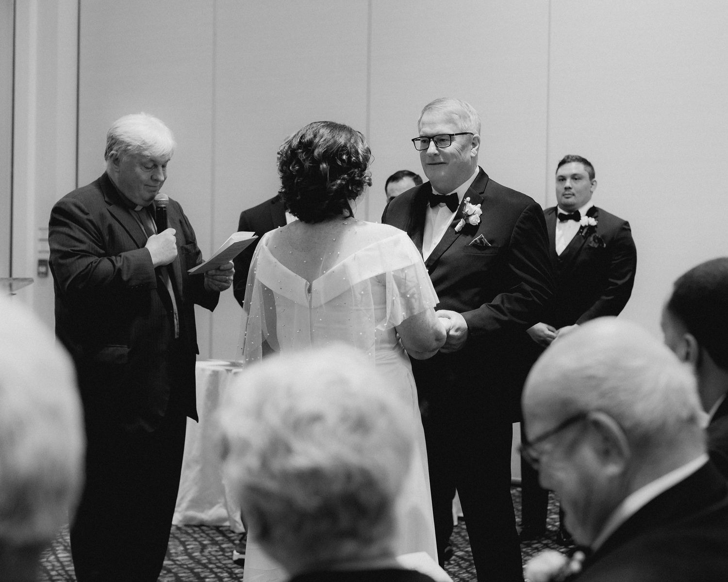 Wedding guests in formal attire gathered for an indoor ceremony.