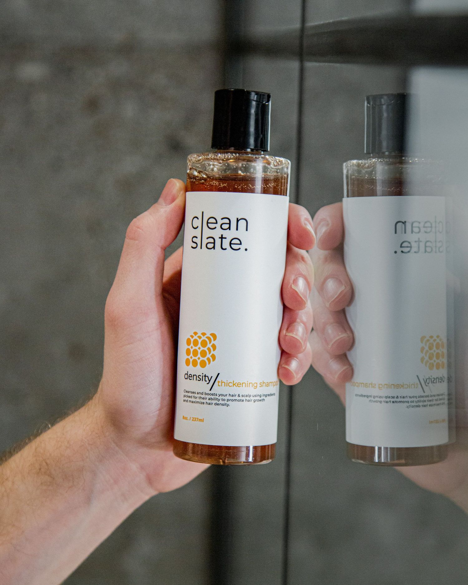 Hands holding clean slate branded skincare bottles against reflective surface.