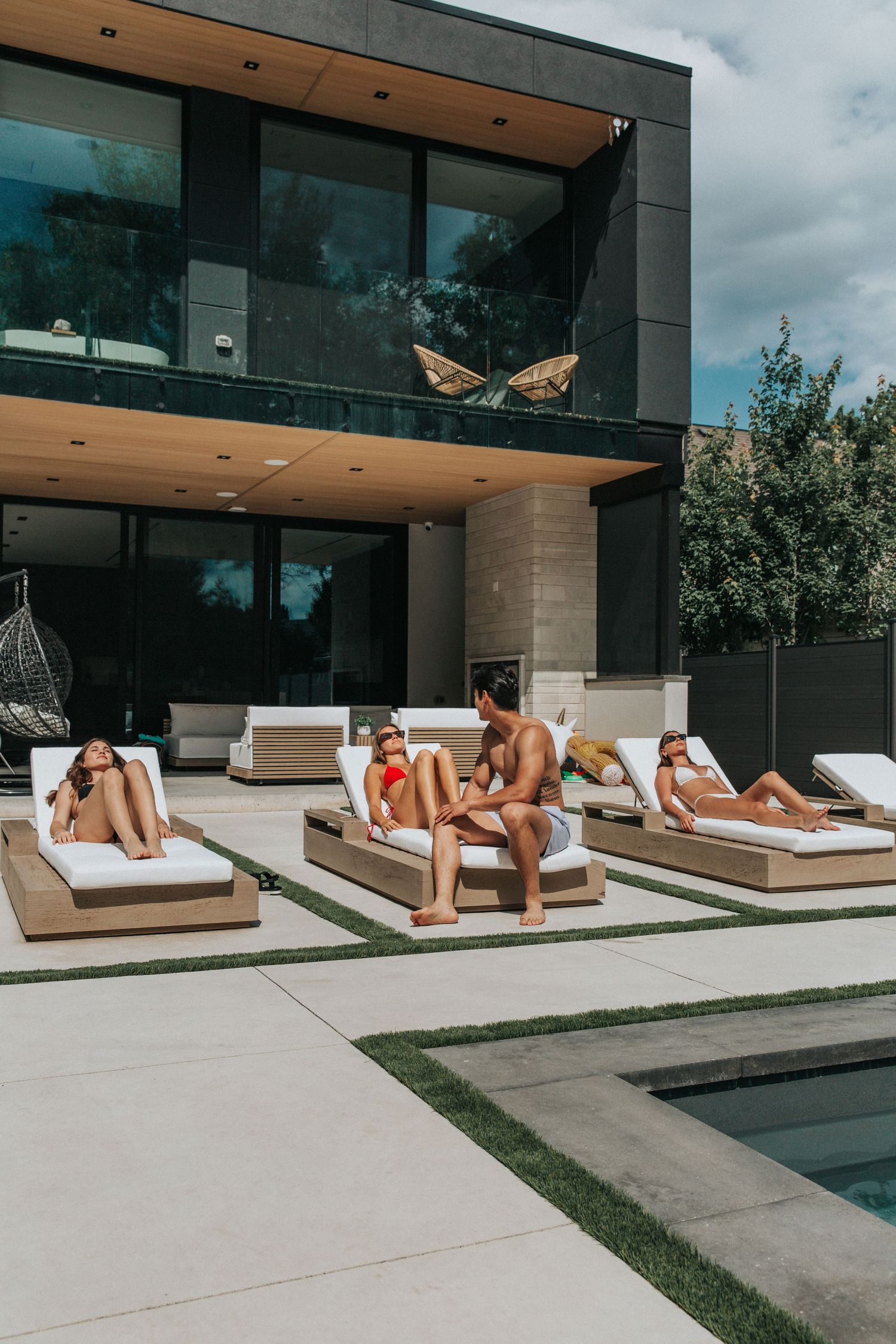 Modern house exterior with pool and lounge chairs where people are relaxing.