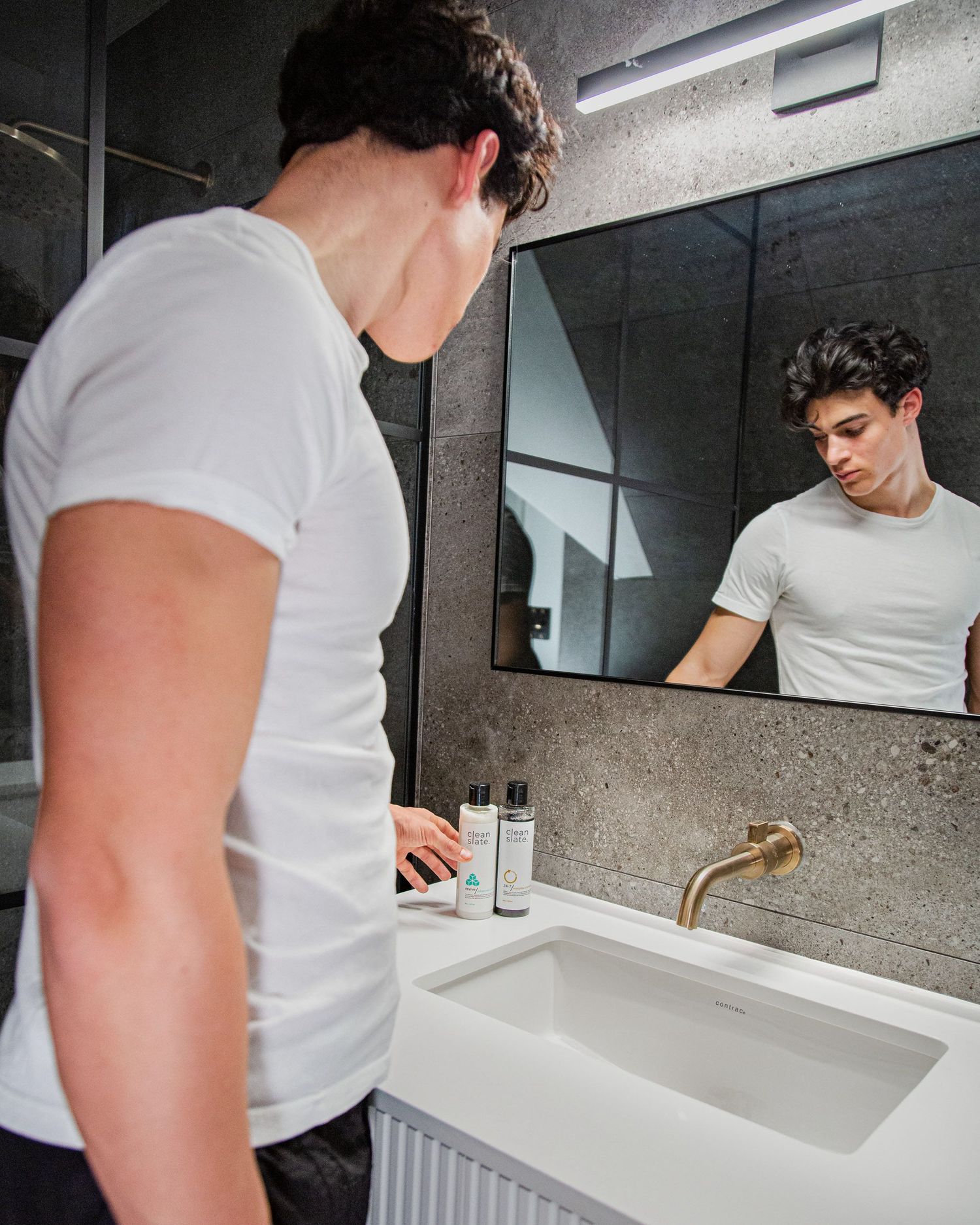 Person in white t-shirt using sink and bathroom products in modern industrial bathroom.
