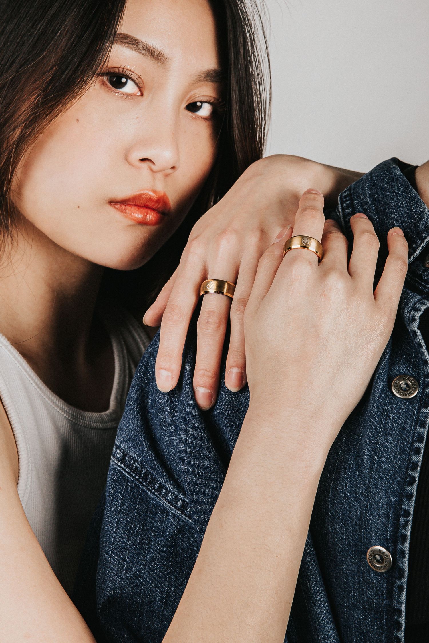 Close-up fashion photo showing hands with gold rings against denim jacket.