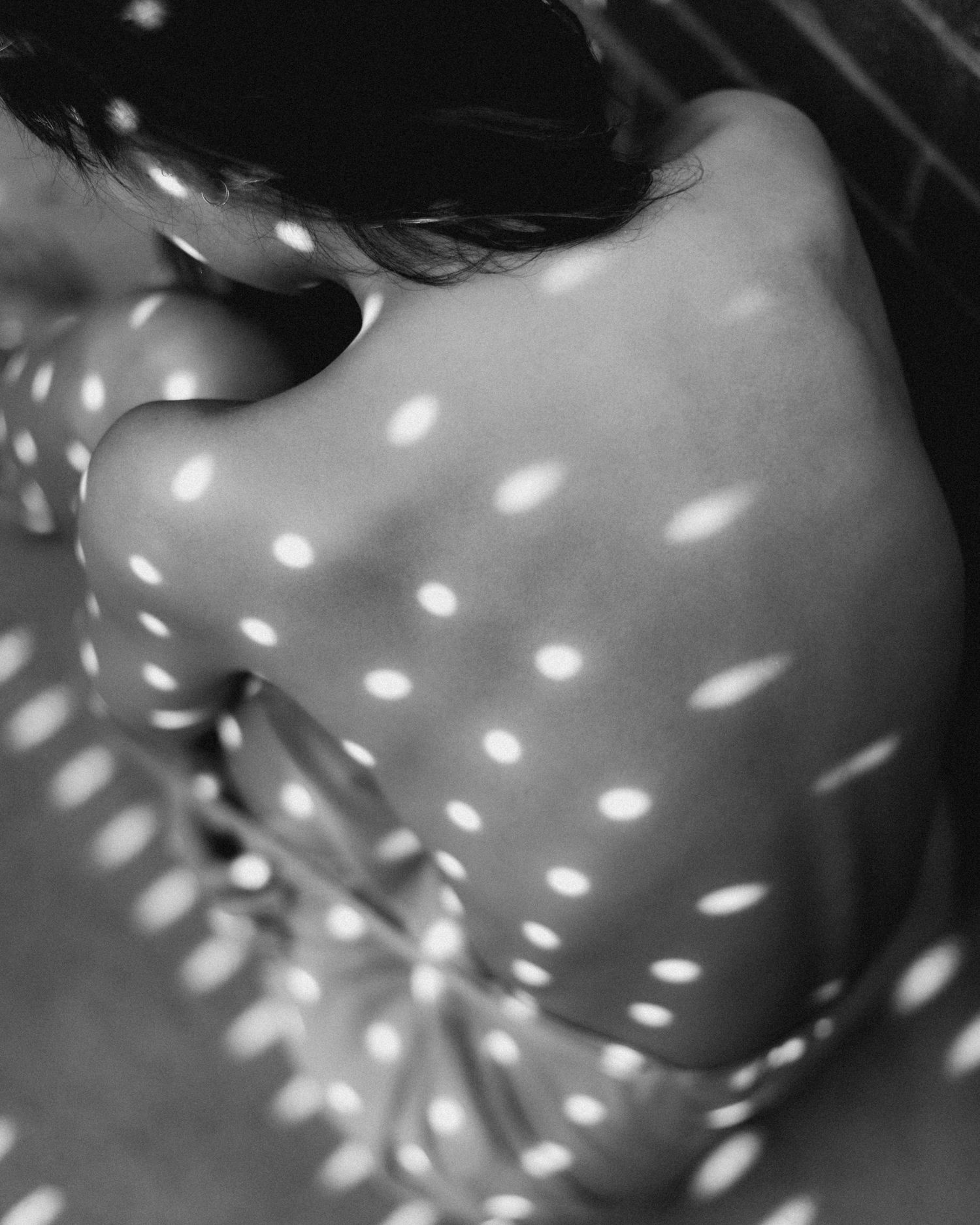 Abstract black and white portrait with dappled light creating spotted pattern effect.