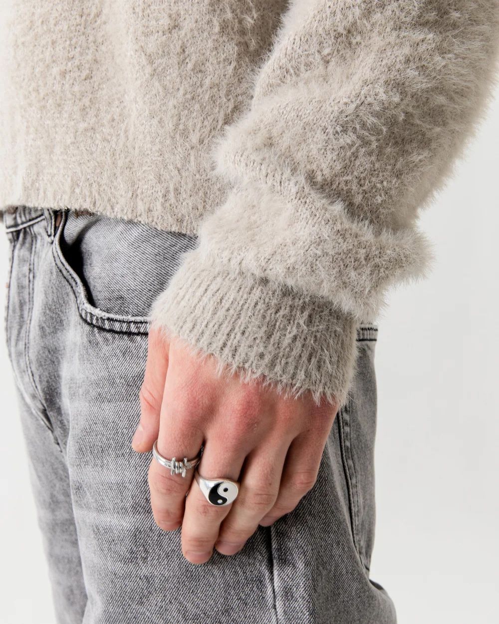 Close-up view of hands wearing a gray fuzzy sweater and rings.