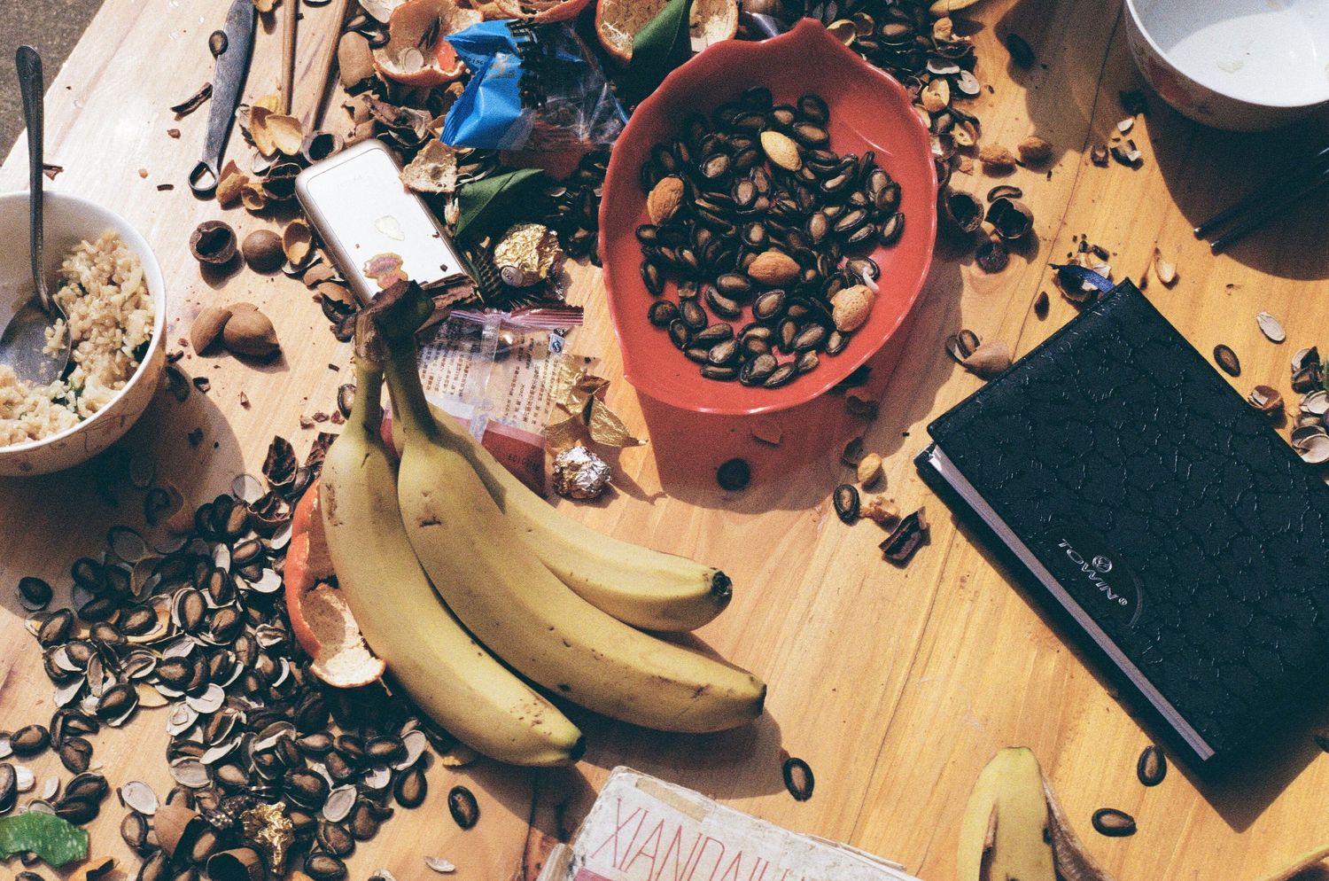 Overhead view of scattered coffee beans and bananas on wooden surface.