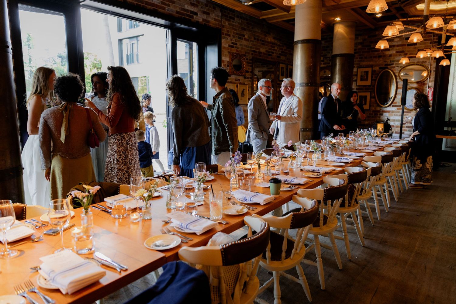 Long dining table set with white linens and wine glasses in a rustic restaurant interior with warm lighting.