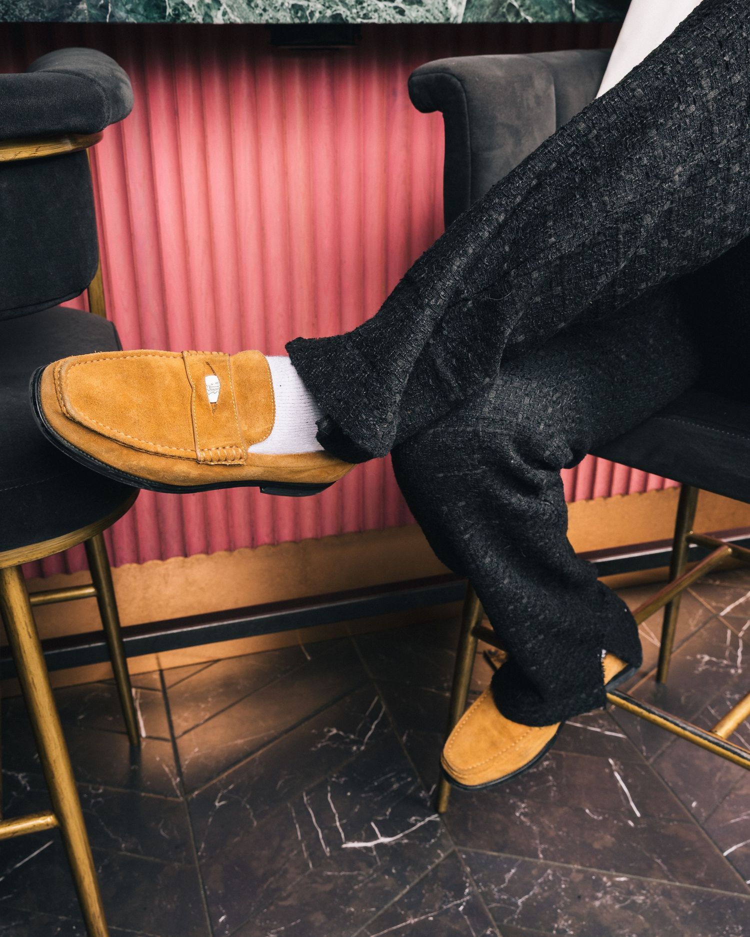 Tan suede shoes shown against dark floor with pink wall.