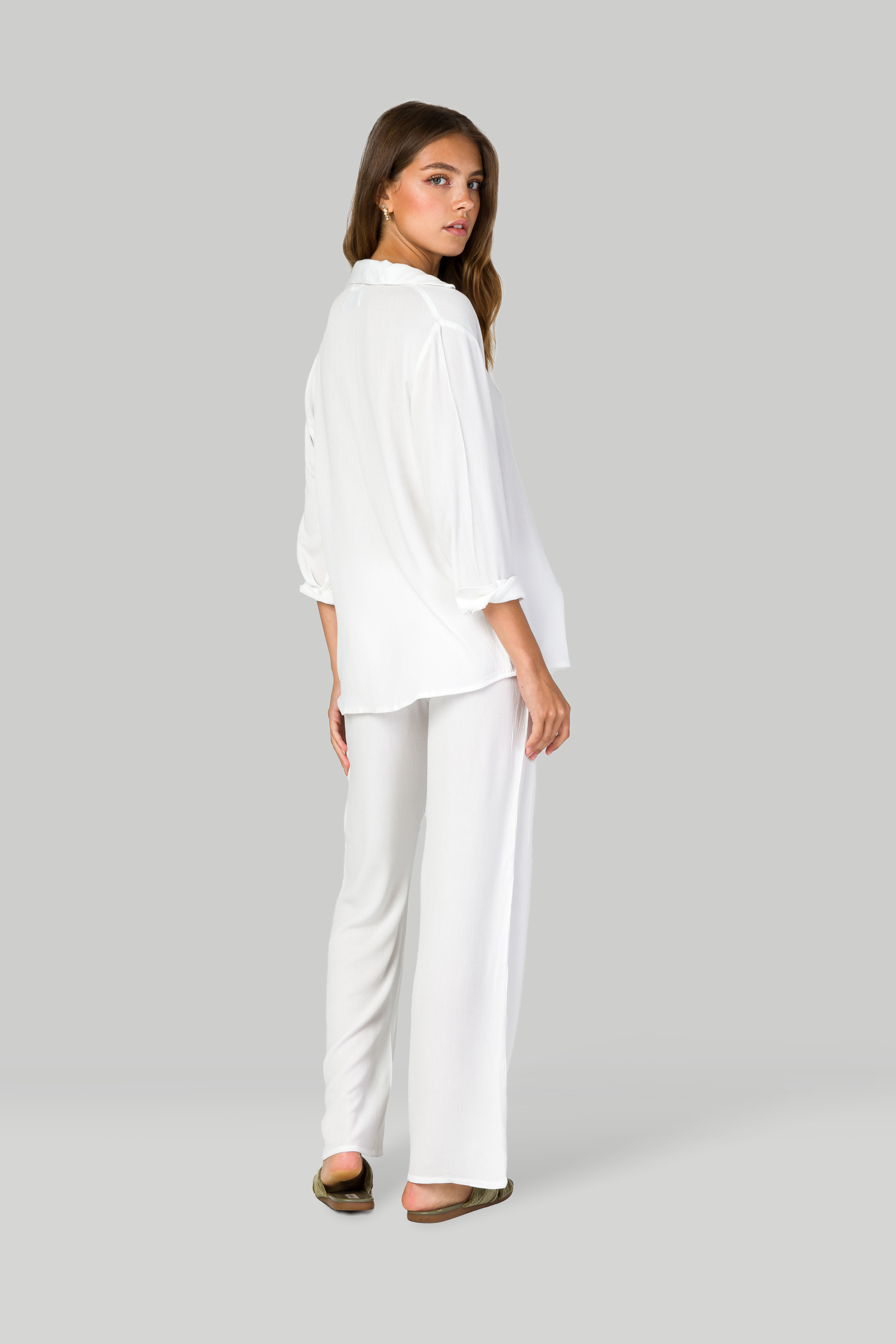 Back view of white shirt and pants outfit with brown sandals on gray background.