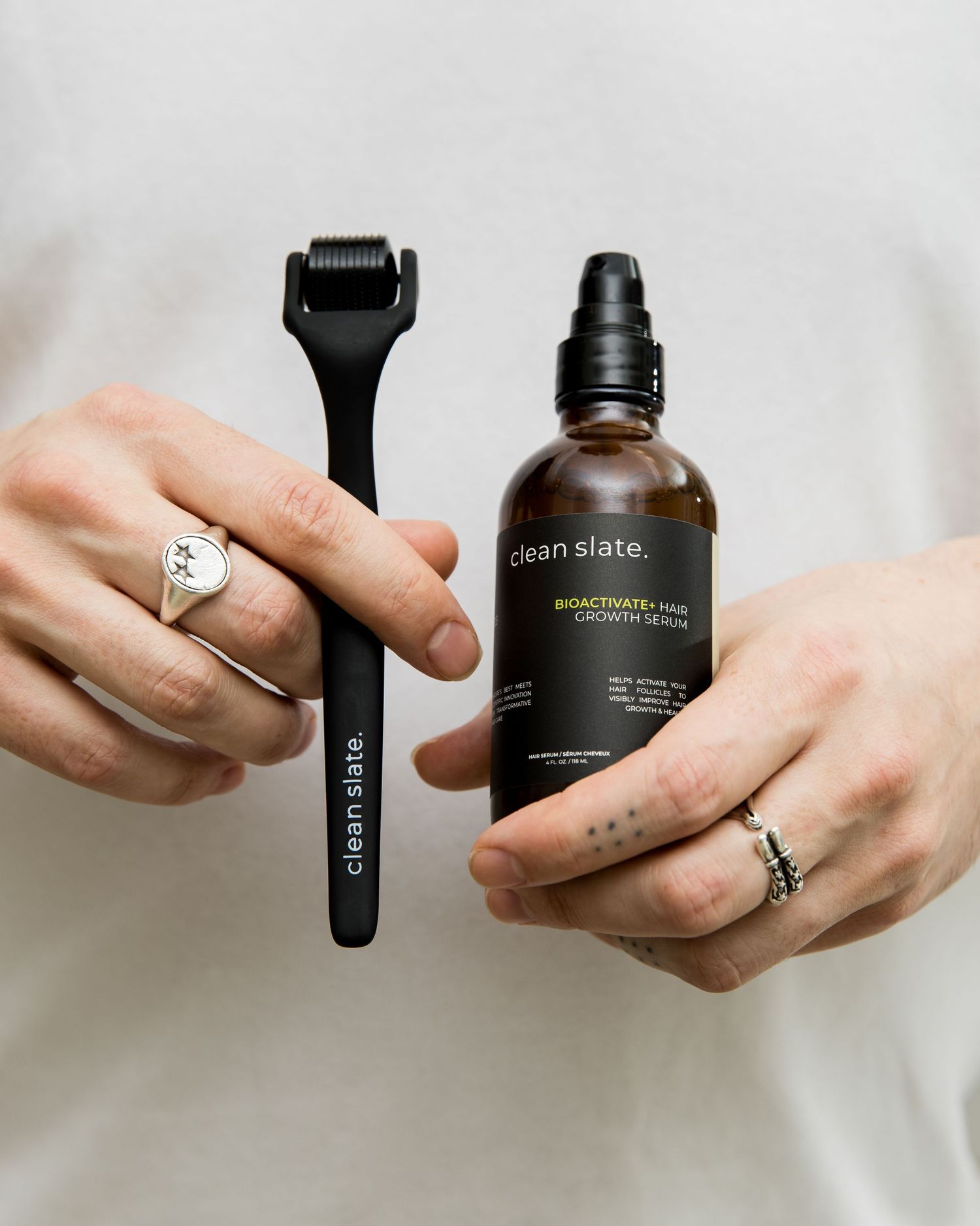 Hands holding and demonstrating Clean Slate beauty product bottles against white background.