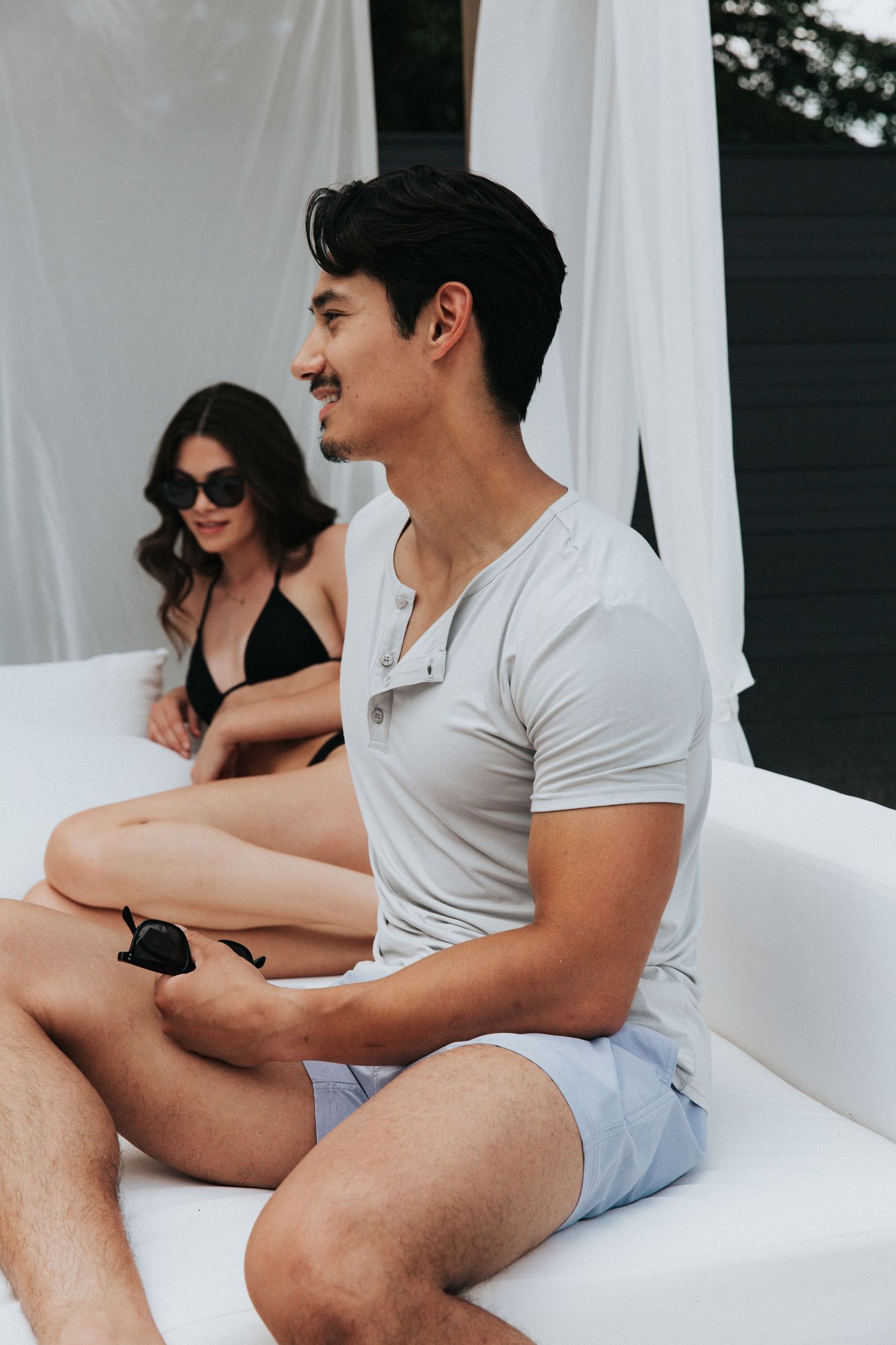 Two people lounging together on white outdoor furniture during daytime.