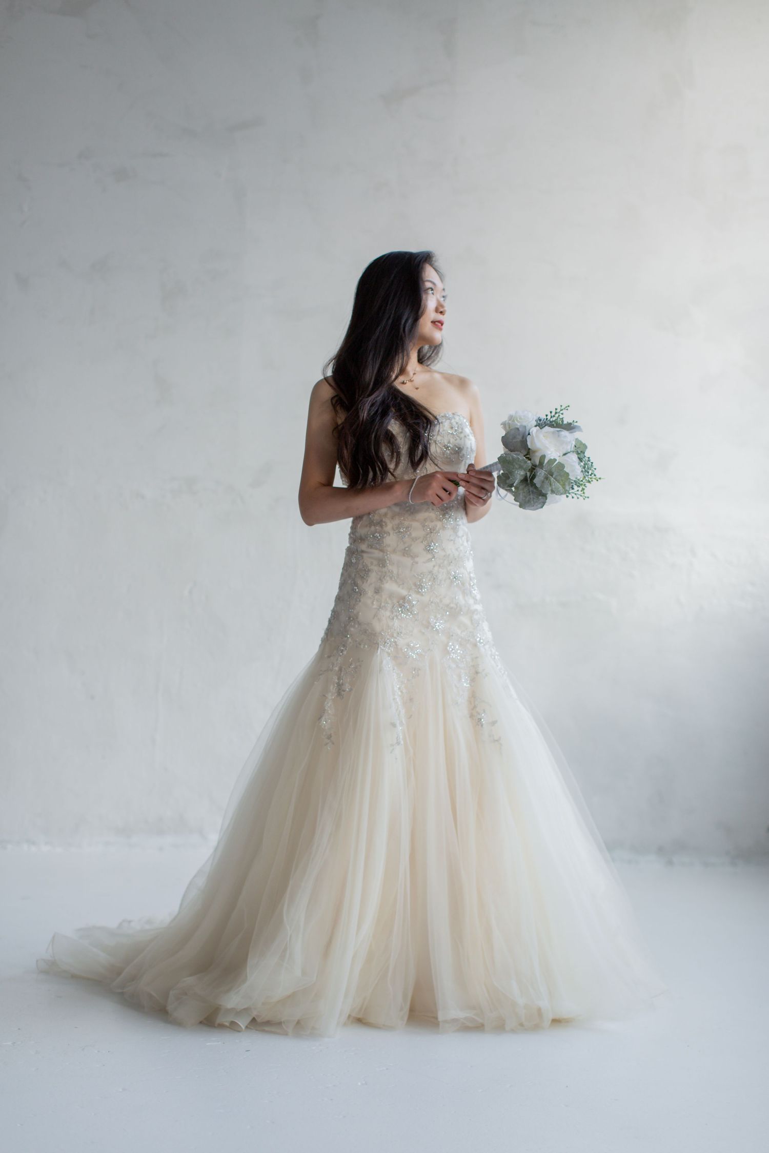 Ethereal bridal portraits in a flowing champagne ballgown against a light gray studio backdrop.