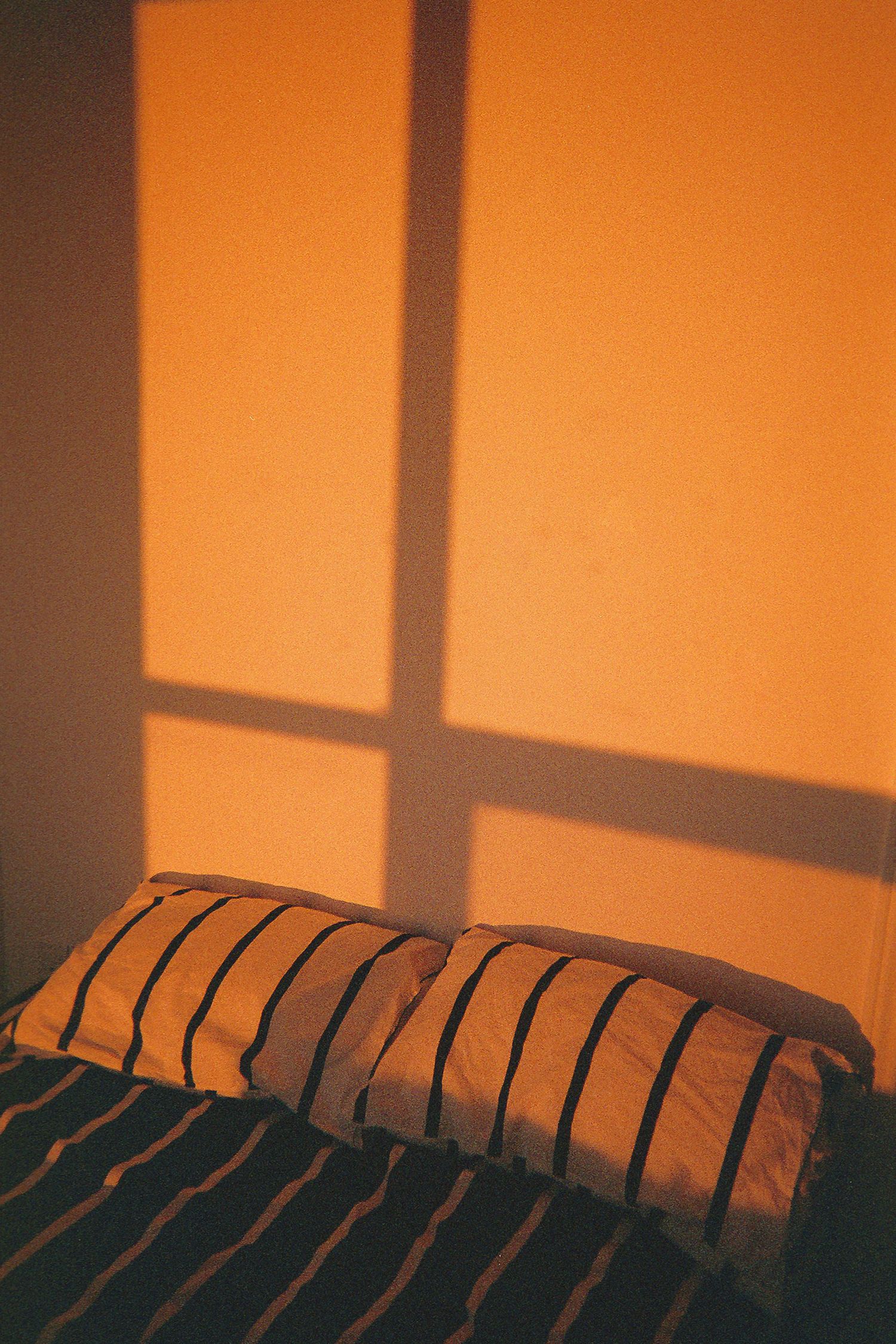 Orange-tinted silhouette of window blinds casting dramatic shadows.