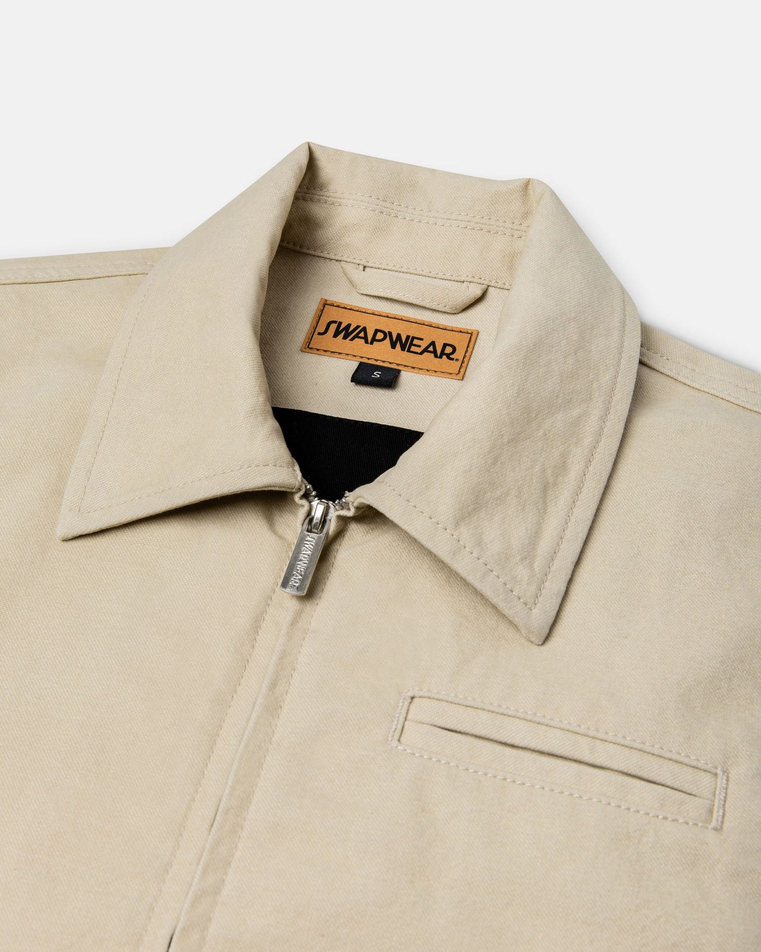 Close-up of a beige zip-up jacket with a spread collar and chest pocket, featuring a SwapWear label.