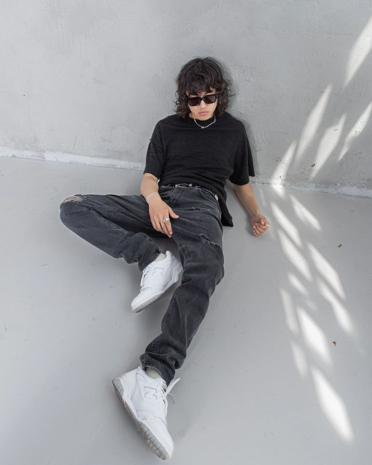 Relaxed poses on grey floor wearing dark denim and white sneakers.