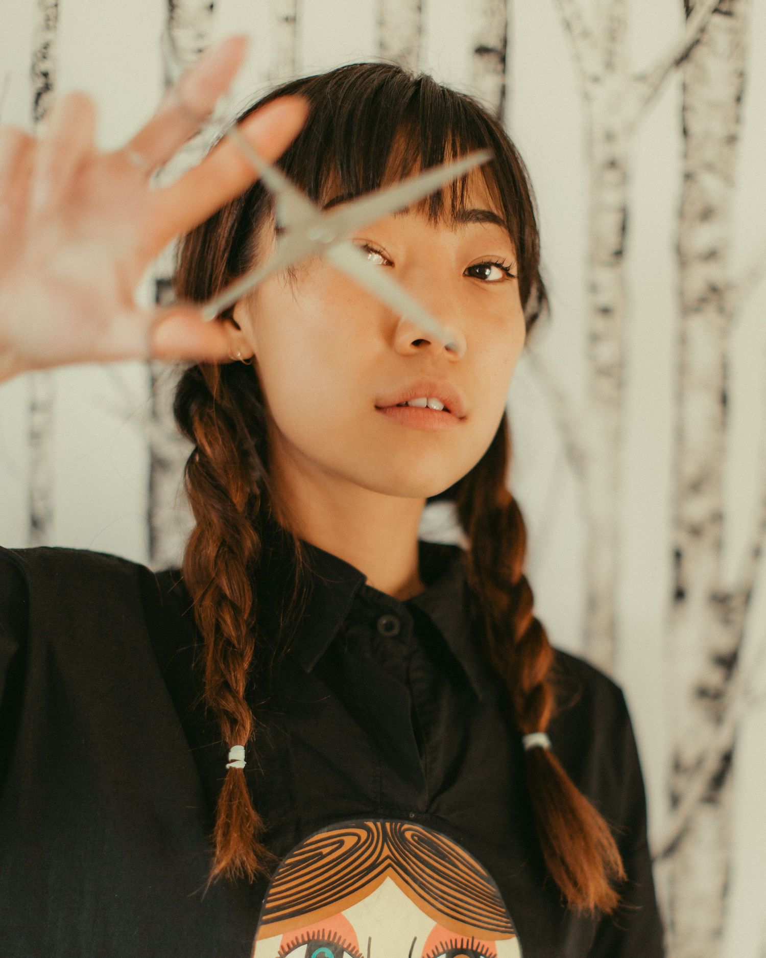 Artistic portrait against birch trees background showing playful expressions and braided hairstyle.