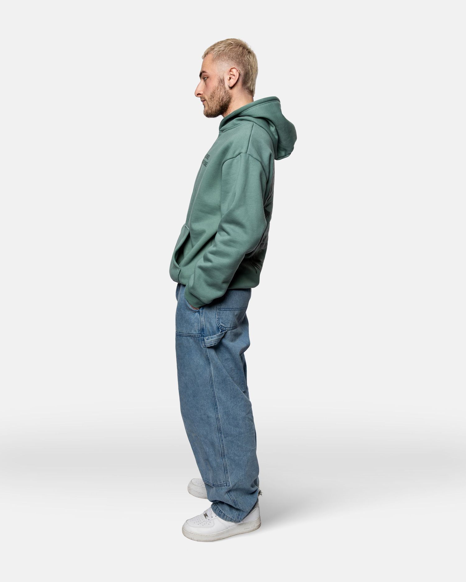 Side views of a person wearing a green hoodie, baggy jeans and white sneakers against a white background.