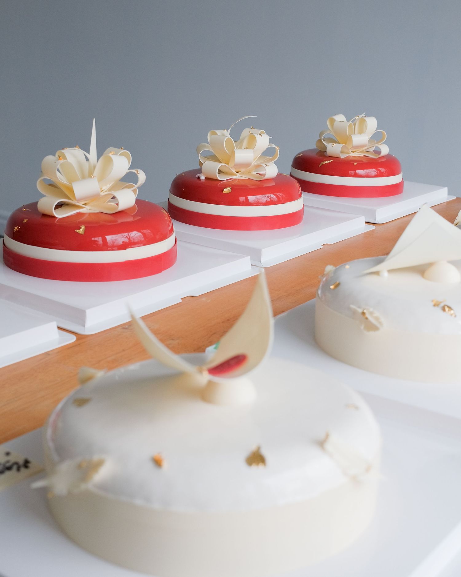 Modern red and white glazed desserts with decorative white chocolate flowers displayed on a wooden board.