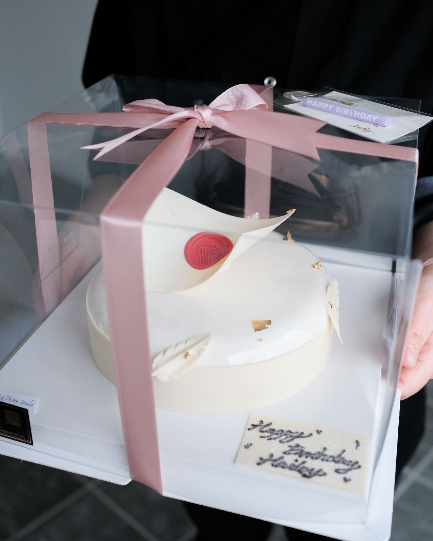 White cake in a clear gift box with pink ribbon and bow packaging.