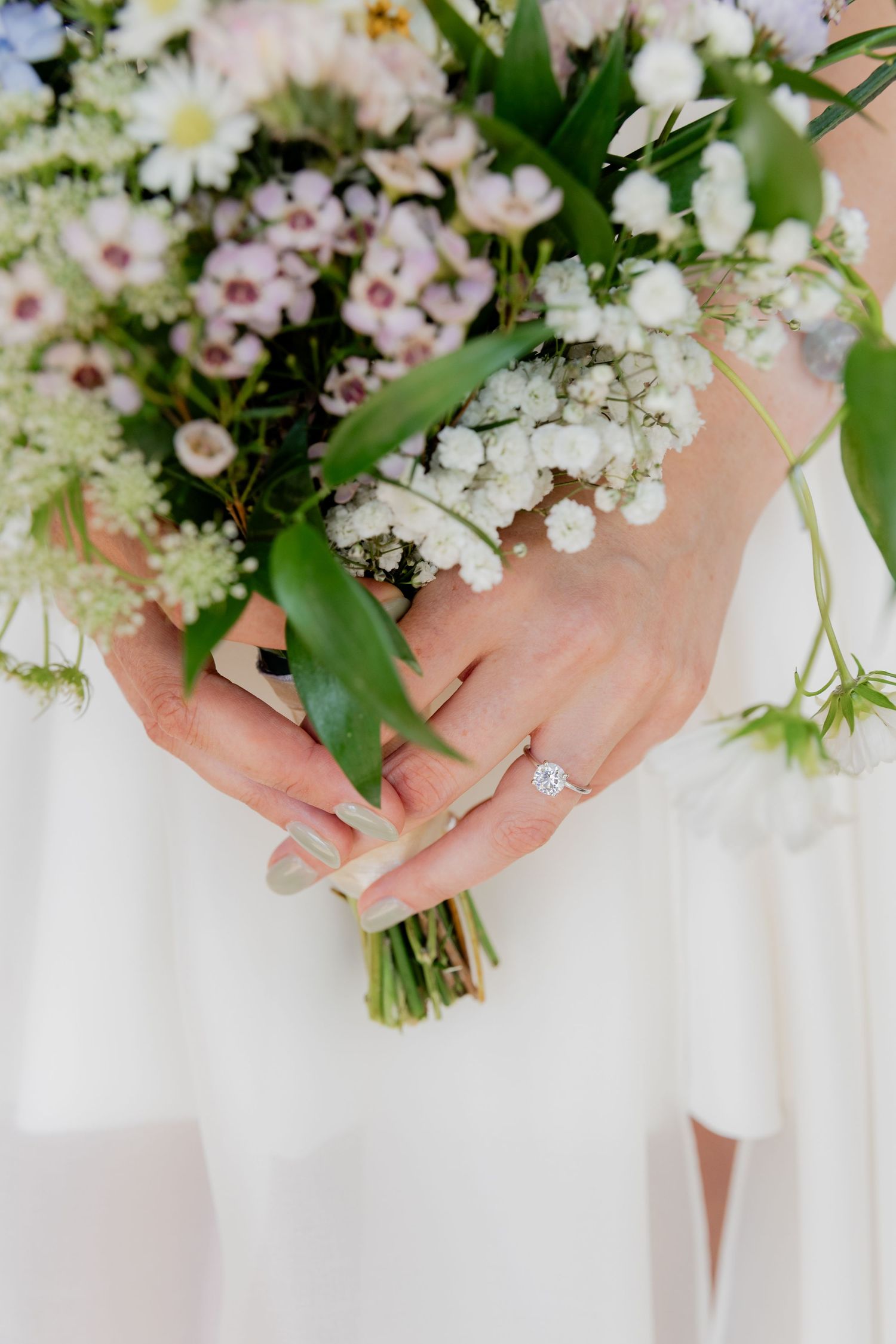 Delicate white and pink spring flowers held in hands against a soft white background.