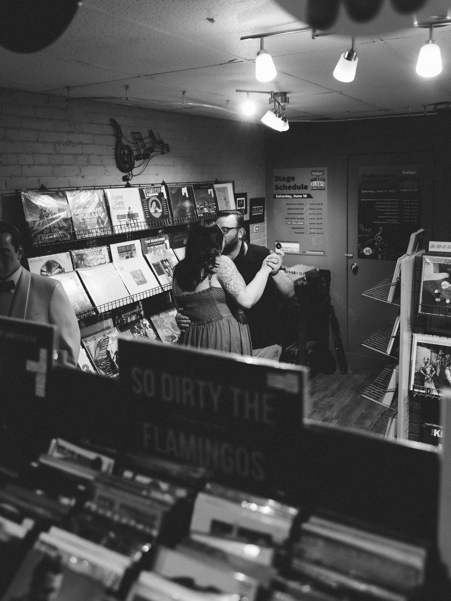 Black and white photo of a couple dancing in a vinyl record shop with a sign reading So Dirty The Flamingos.