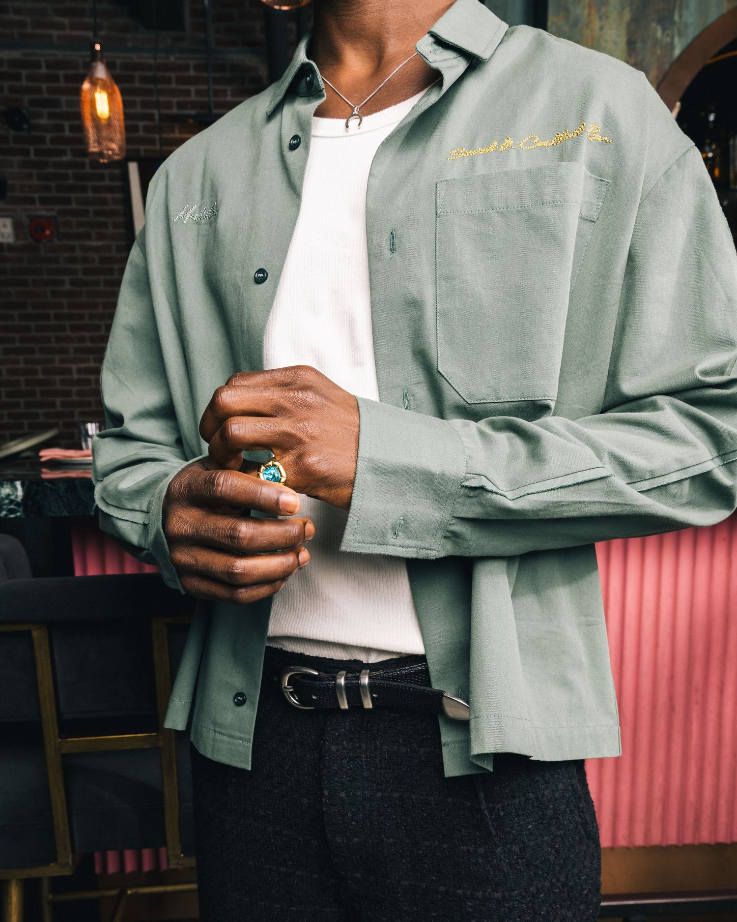 Person wearing sage green jacket and white shirt shown from torso down in stylish casual outfit.