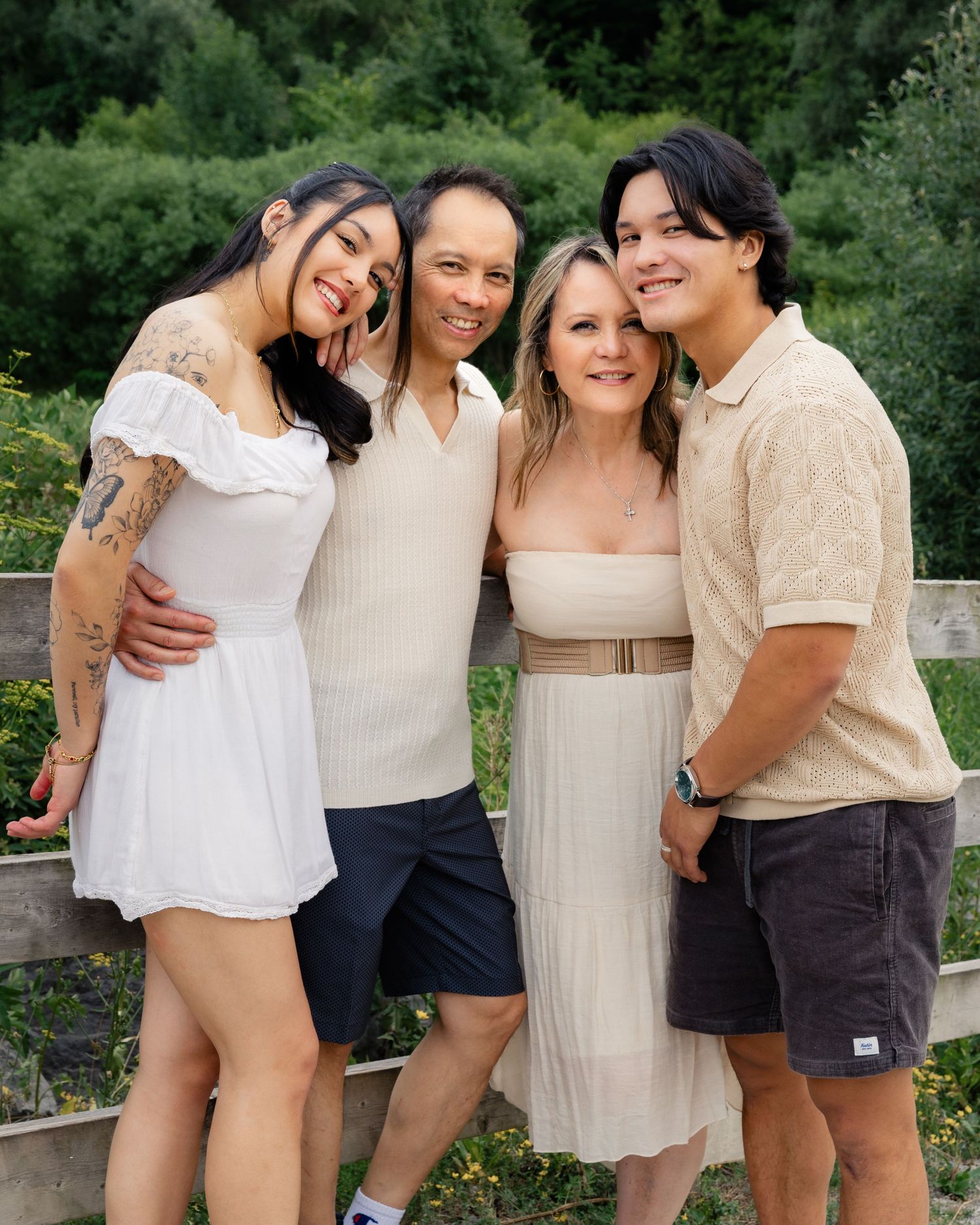 Group of friends in neutral colored outfits laughing and embracing outdoors in a garden setting.