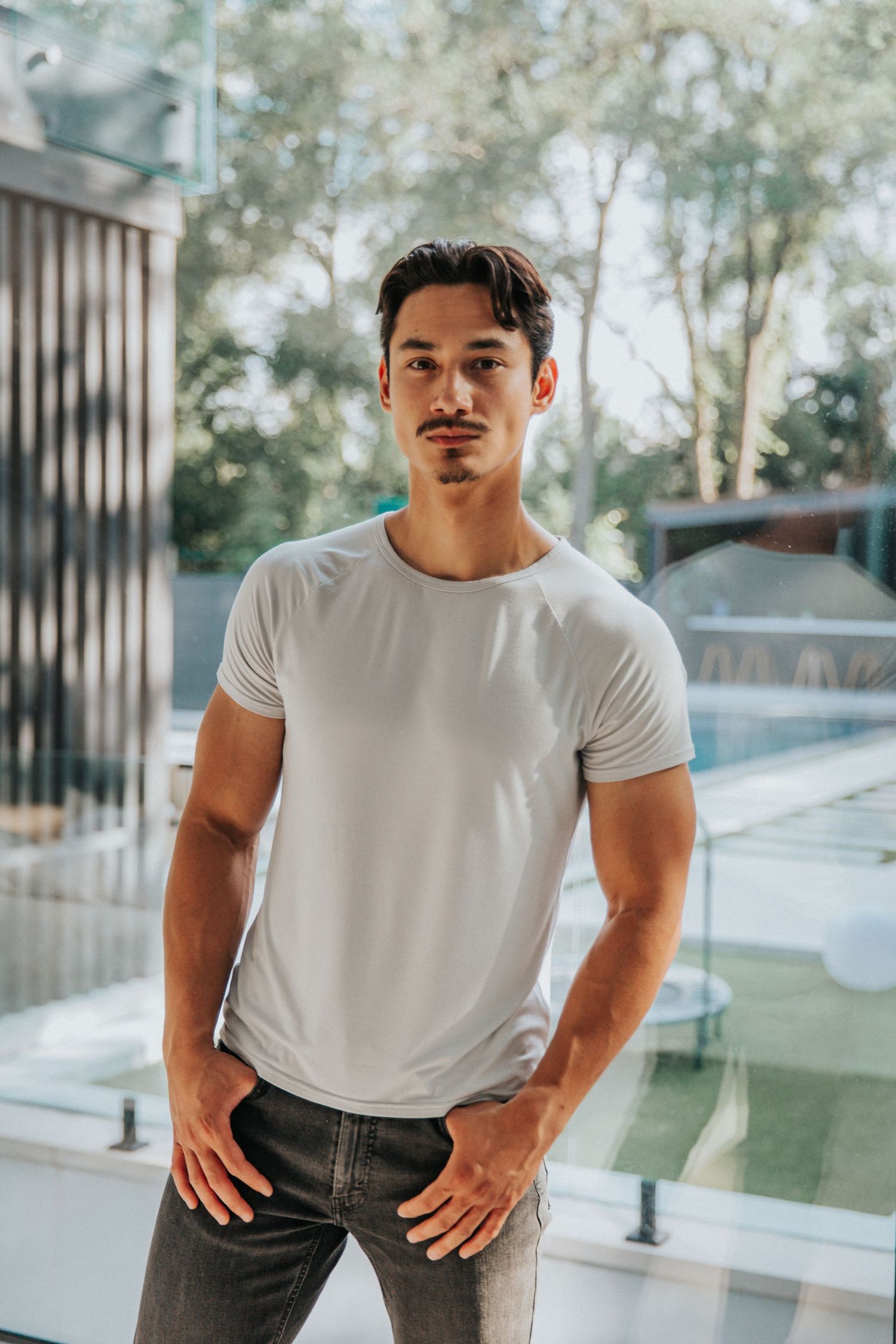Person in white t-shirt and jeans posing against modern architectural backdrop.