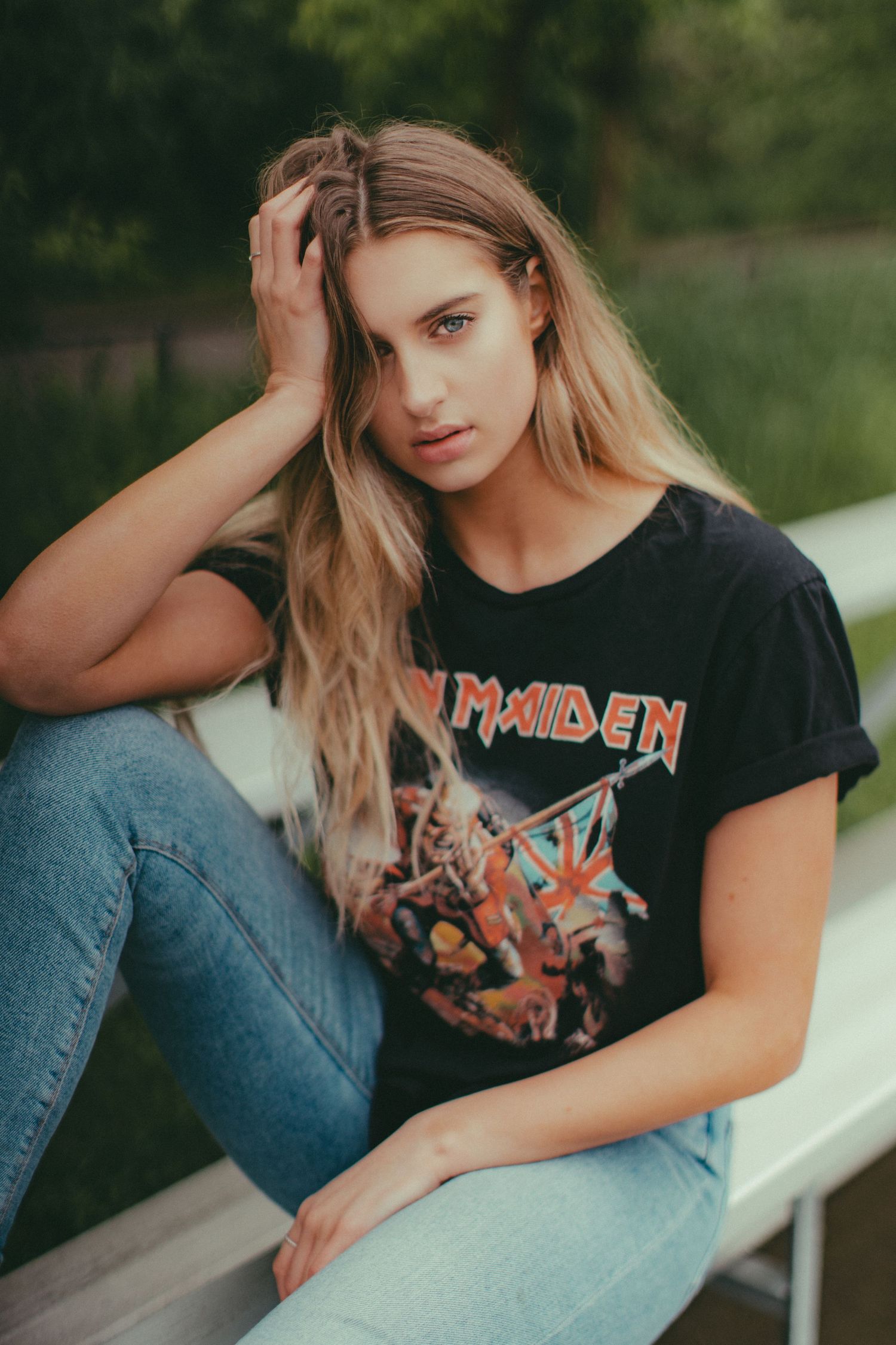 Outdoor portrait wearing Iron Maiden band t-shirt while sitting on white bench.