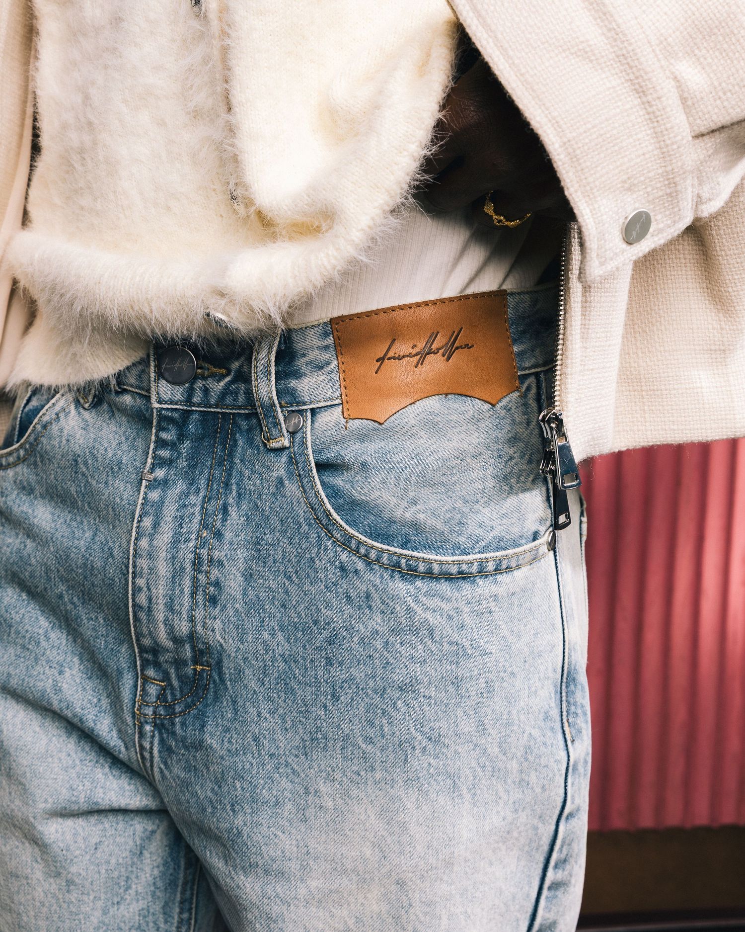 Detail of light wash denim jeans with small tattoo visible near pocket.