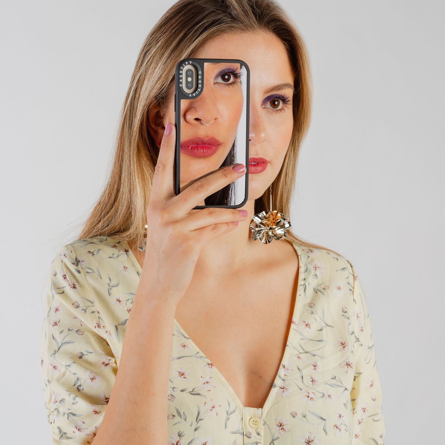 Woman in floral dress taking selfies with smartphone against white background.