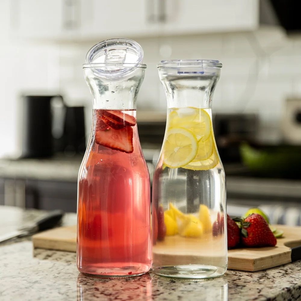 Glass carafes with pink and yellow infused beverages arranged on a marble countertop.