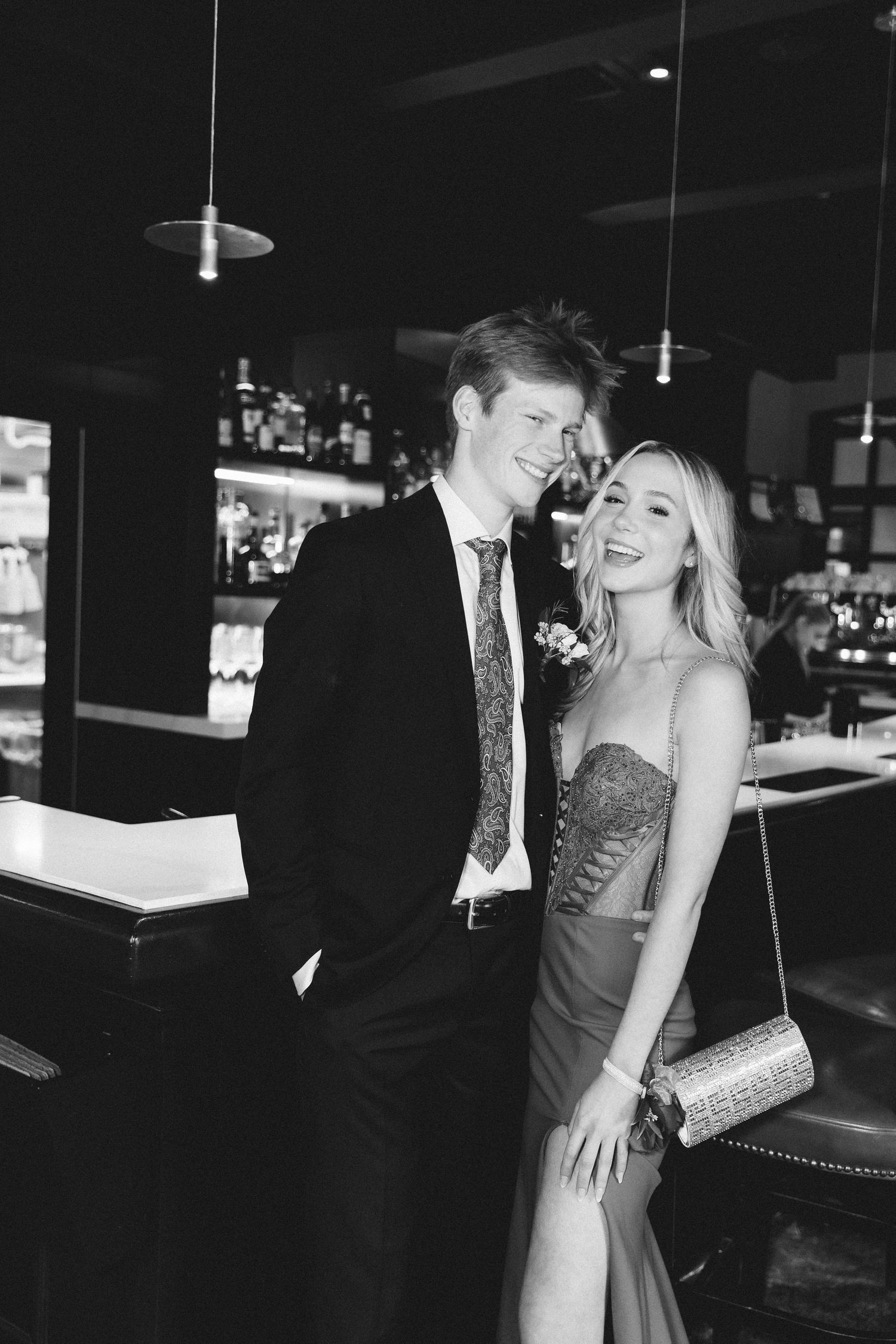 Black and white photo of a smiling couple dressed formally, posing together in an elegant bar setting.
