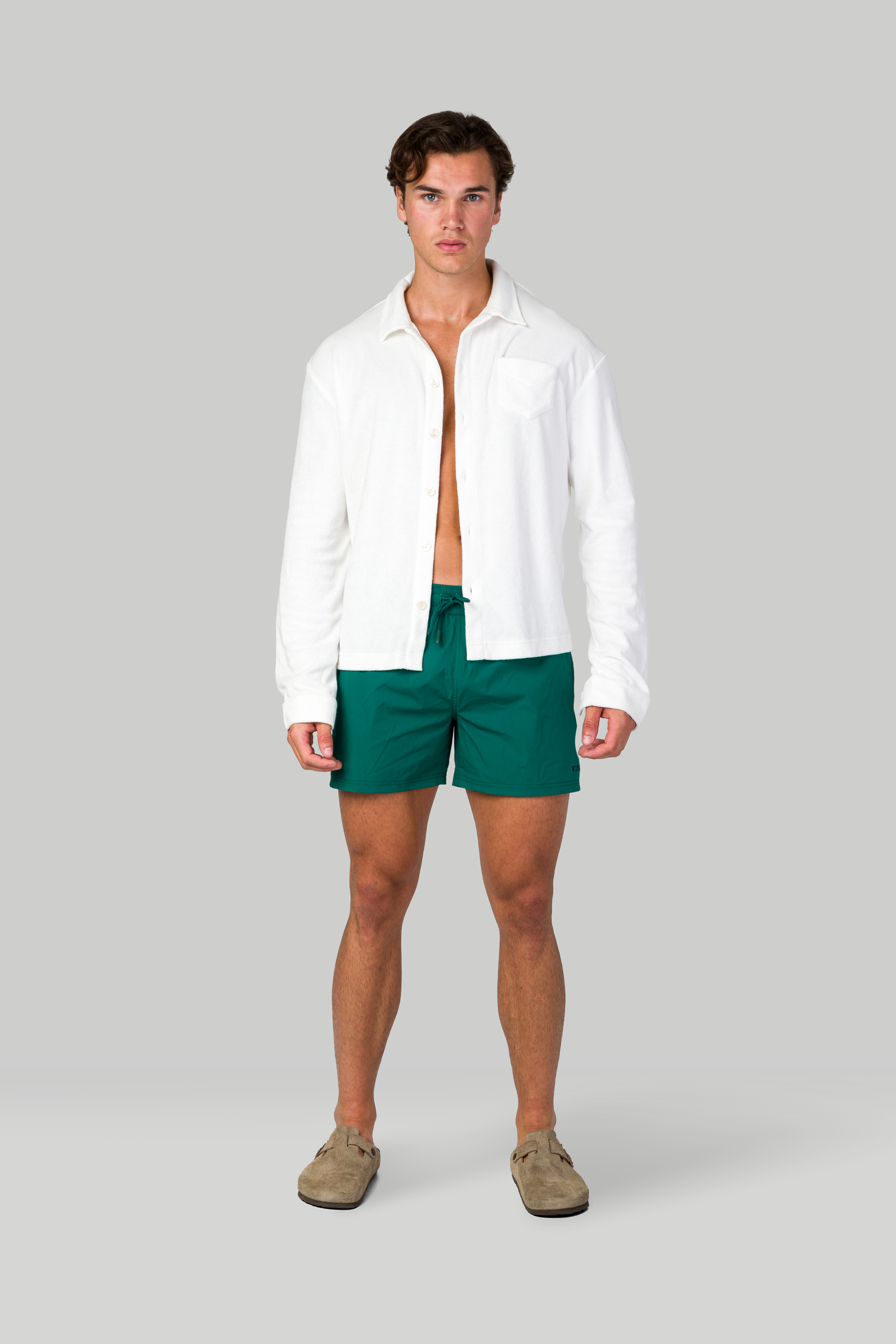 White button-down shirt and green swim shorts outfit with beige loafers on gray background.