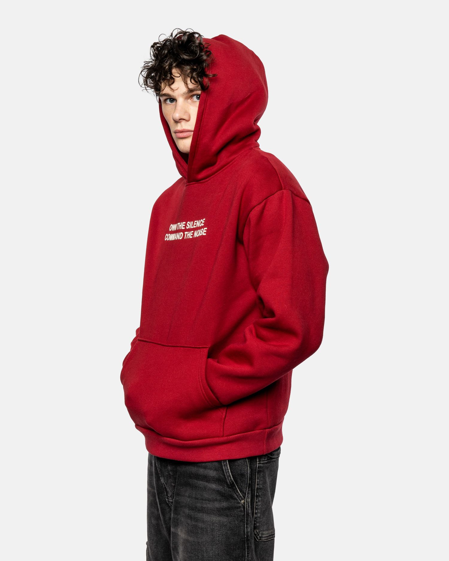 Someone wearing a bright red hoodie sweatshirt with text and dark jeans poses against a white background.
